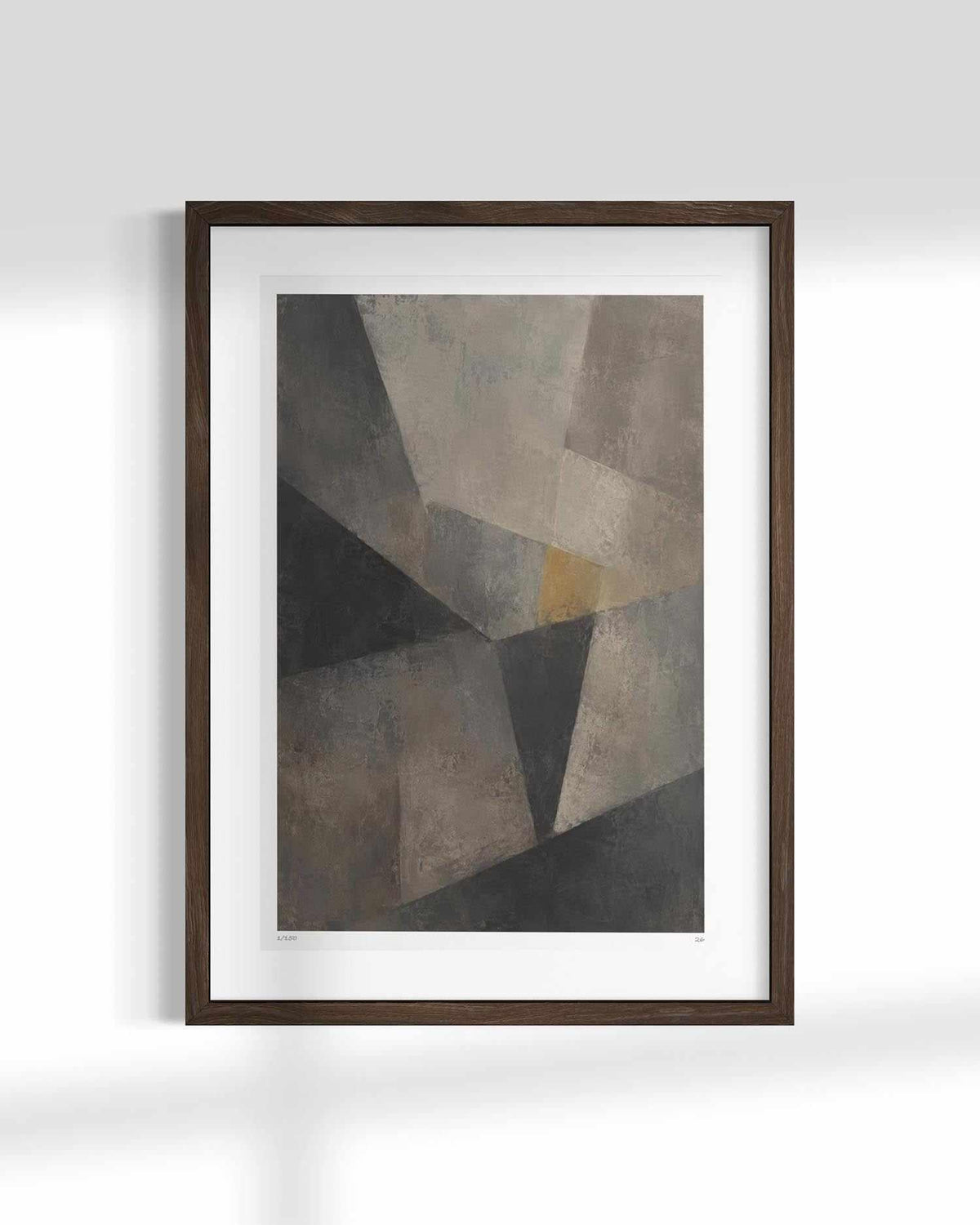 Framed abstract geometric wall art featuring textured gray, black, and taupe shapes with a small warm gold accent, displayed in a dark wood frame with a white mat against a light gray wall.