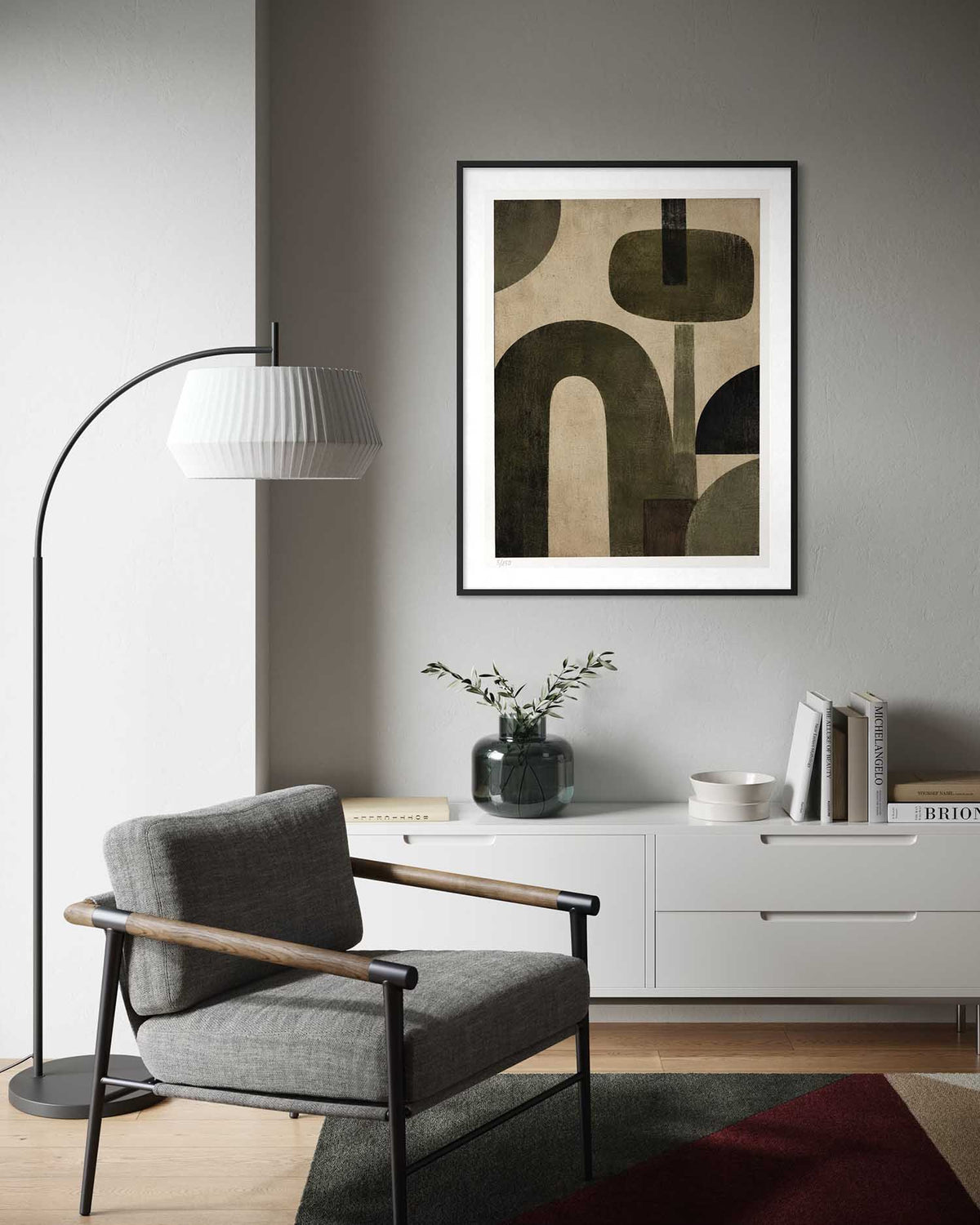 A framed abstract art print with geometric shapes in beige, olive green, and black, displayed on a gray wall above a white sideboard in a modern living room setting.