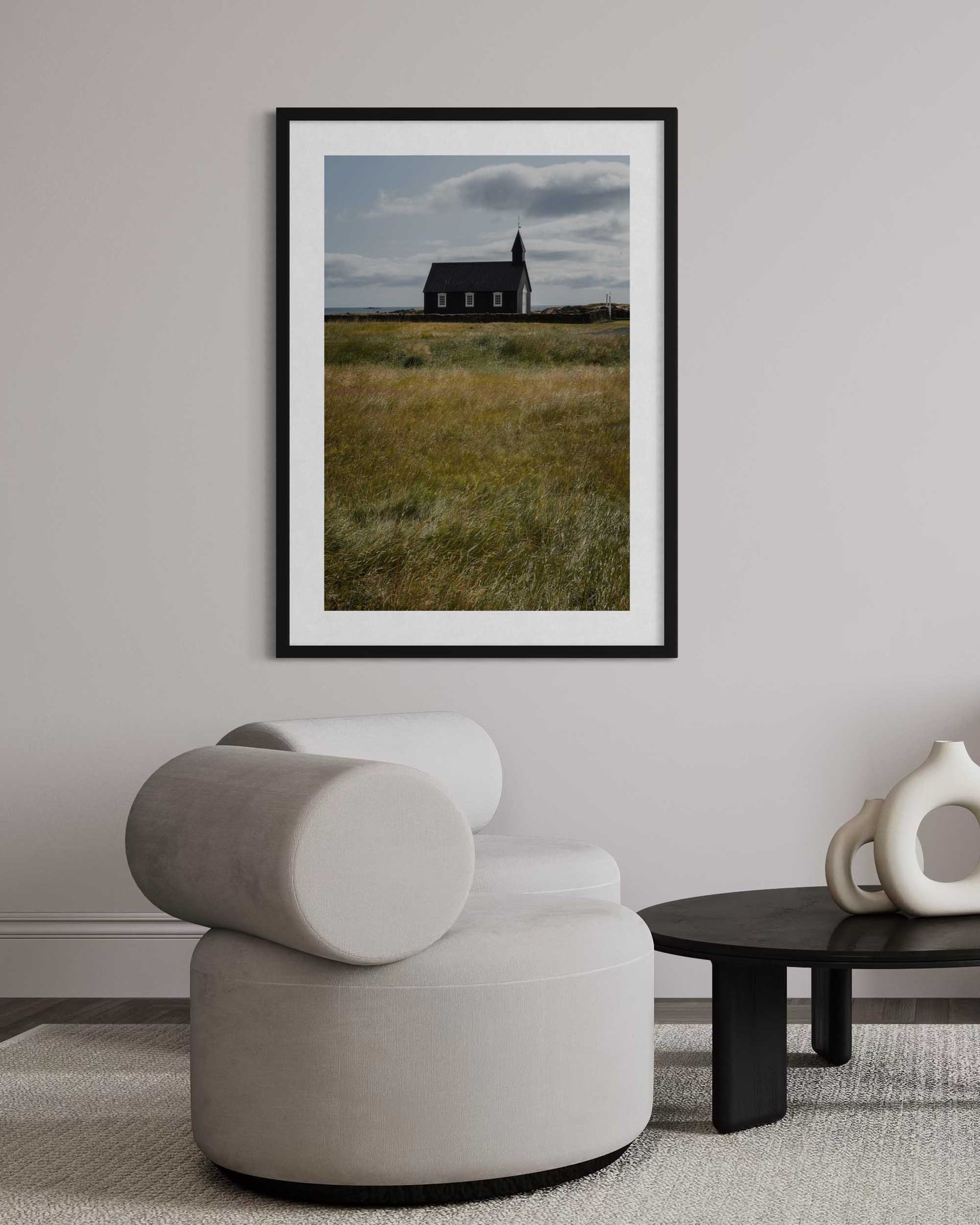 Framed photograph of a church in a field above a modern chair in a room.