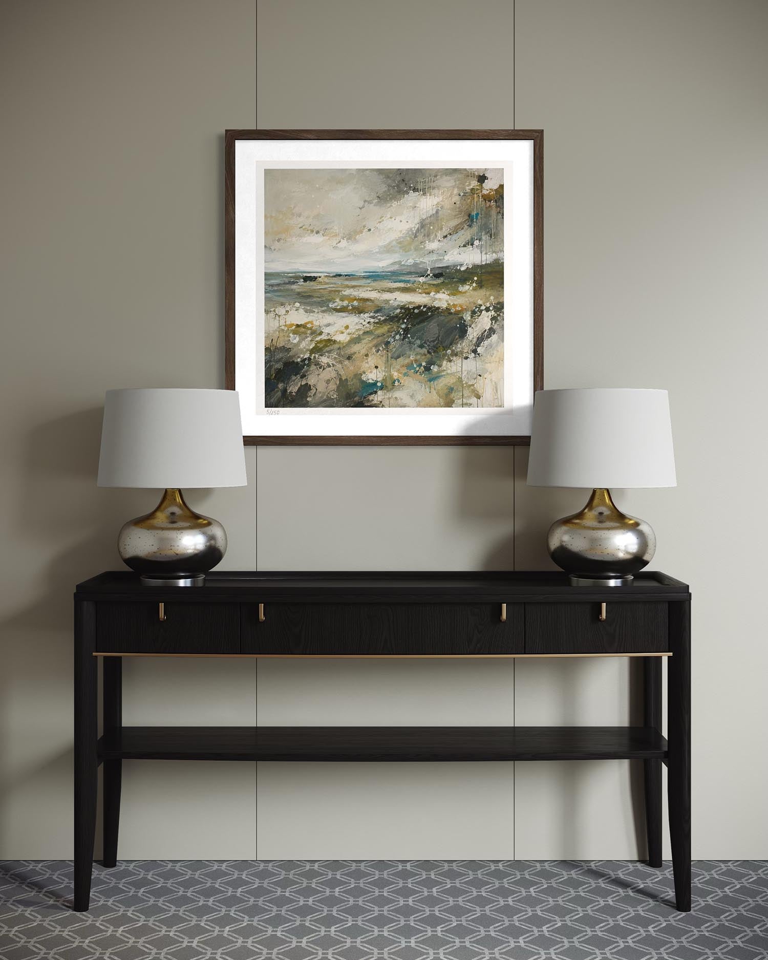 A framed abstract landscape painting in earthy tones hangs on a light gray wall above a black console table with two matching silver and white table lamps.