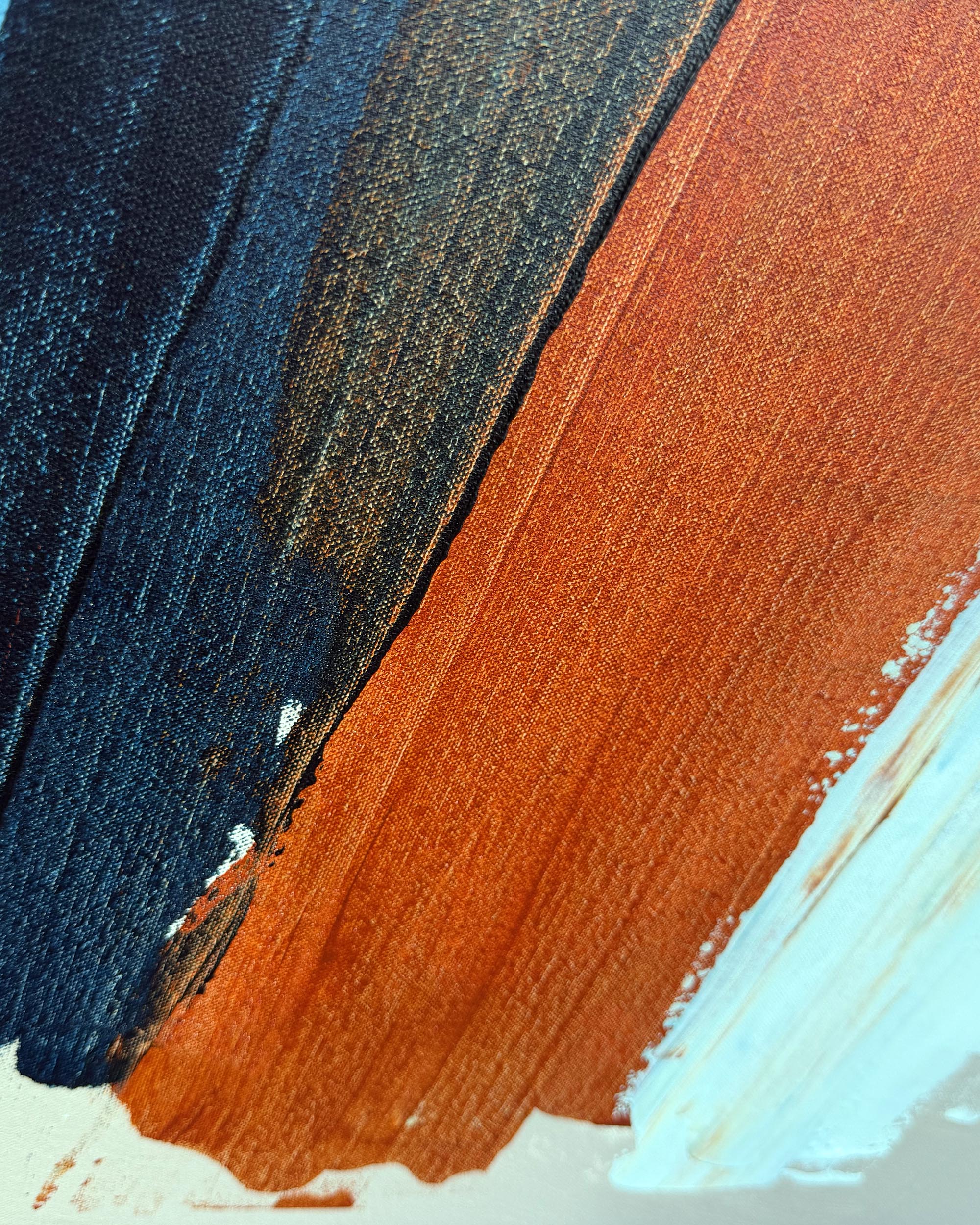 Abstract painted brushstrokes in dark navy blue, warm rust orange, and pale icy blue on a textured canvas surface.