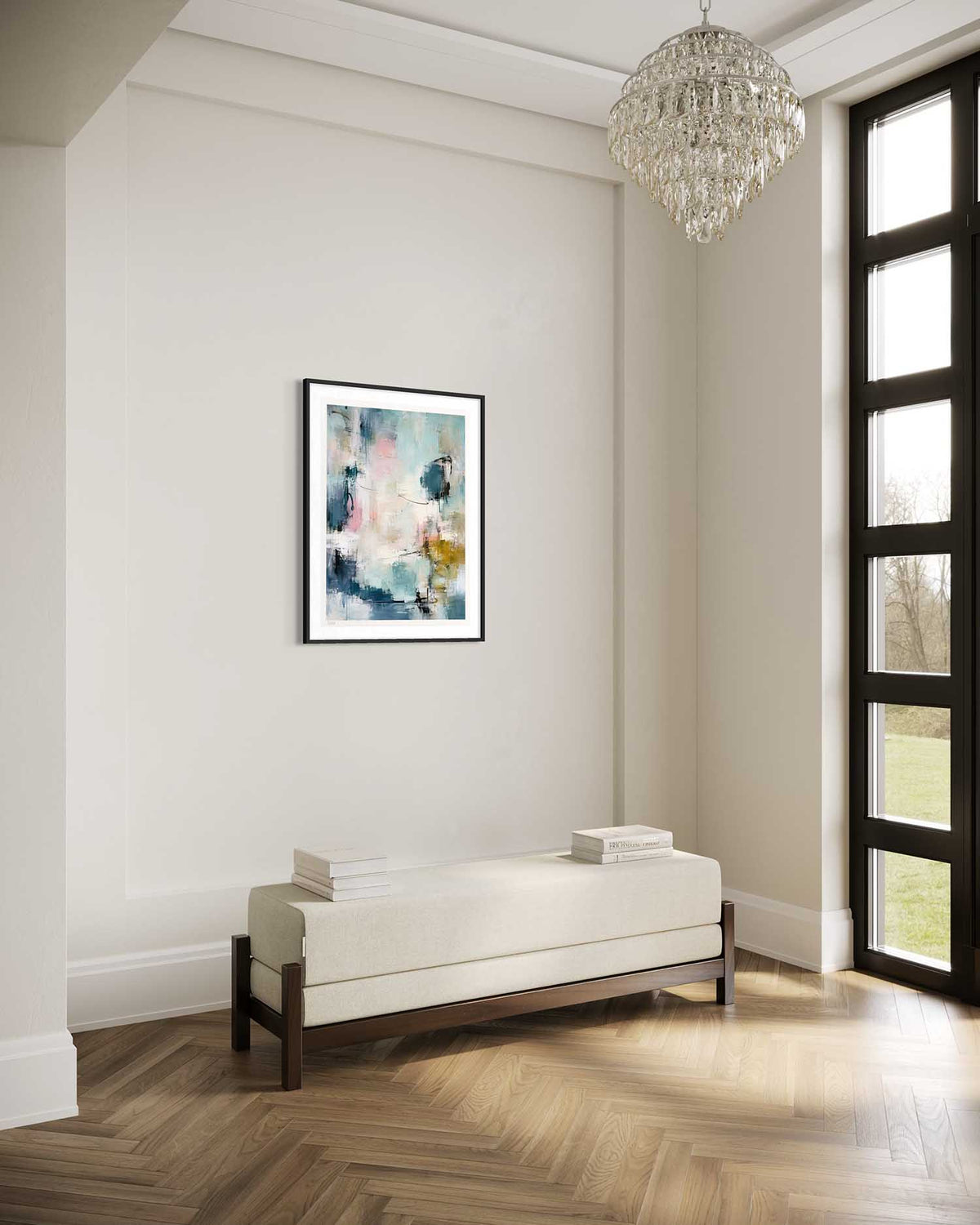 A framed abstract art print with blue, green, and white brushstrokes hangs on a light beige wall in a bright room with a cream upholstered bench, wood herringbone floor, and a large window.