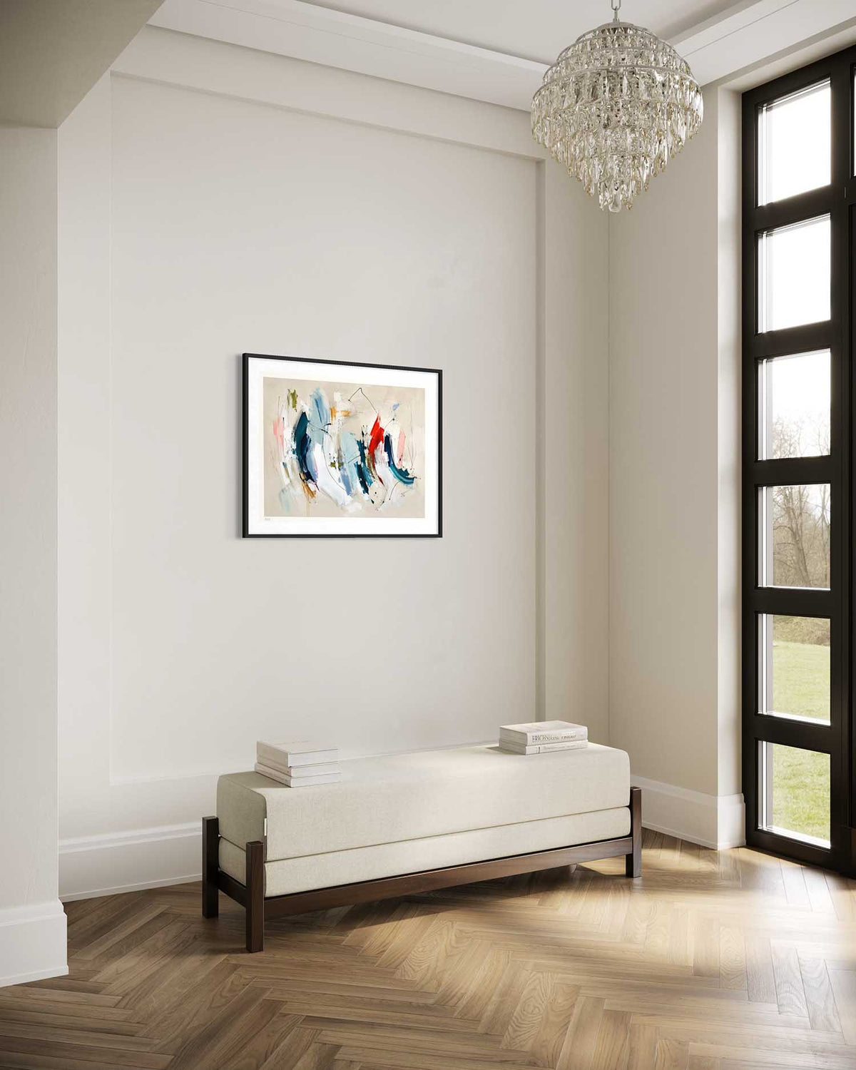 A framed abstract art print featuring blue, red, and white brushstrokes on a beige background, displayed on a light gray wall in a modern living room setting with a white bench, wood herringbone floor, and a crystal chandelier.