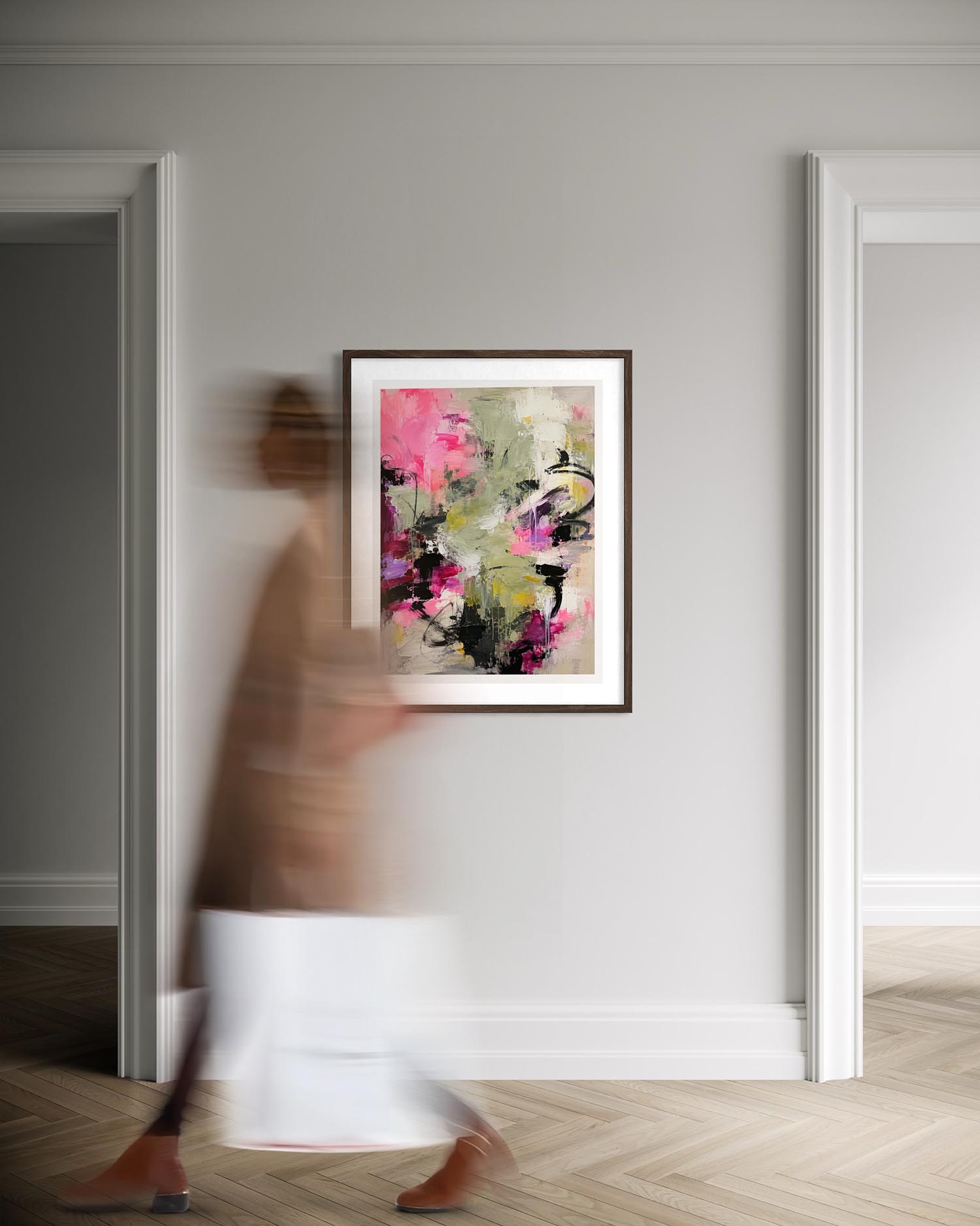 A framed abstract floral painting with vibrant pink, green, and black brushstrokes hangs on a light gray wall in a hallway. A blurred person walks past in the foreground, and two doorway frames flank the wall.