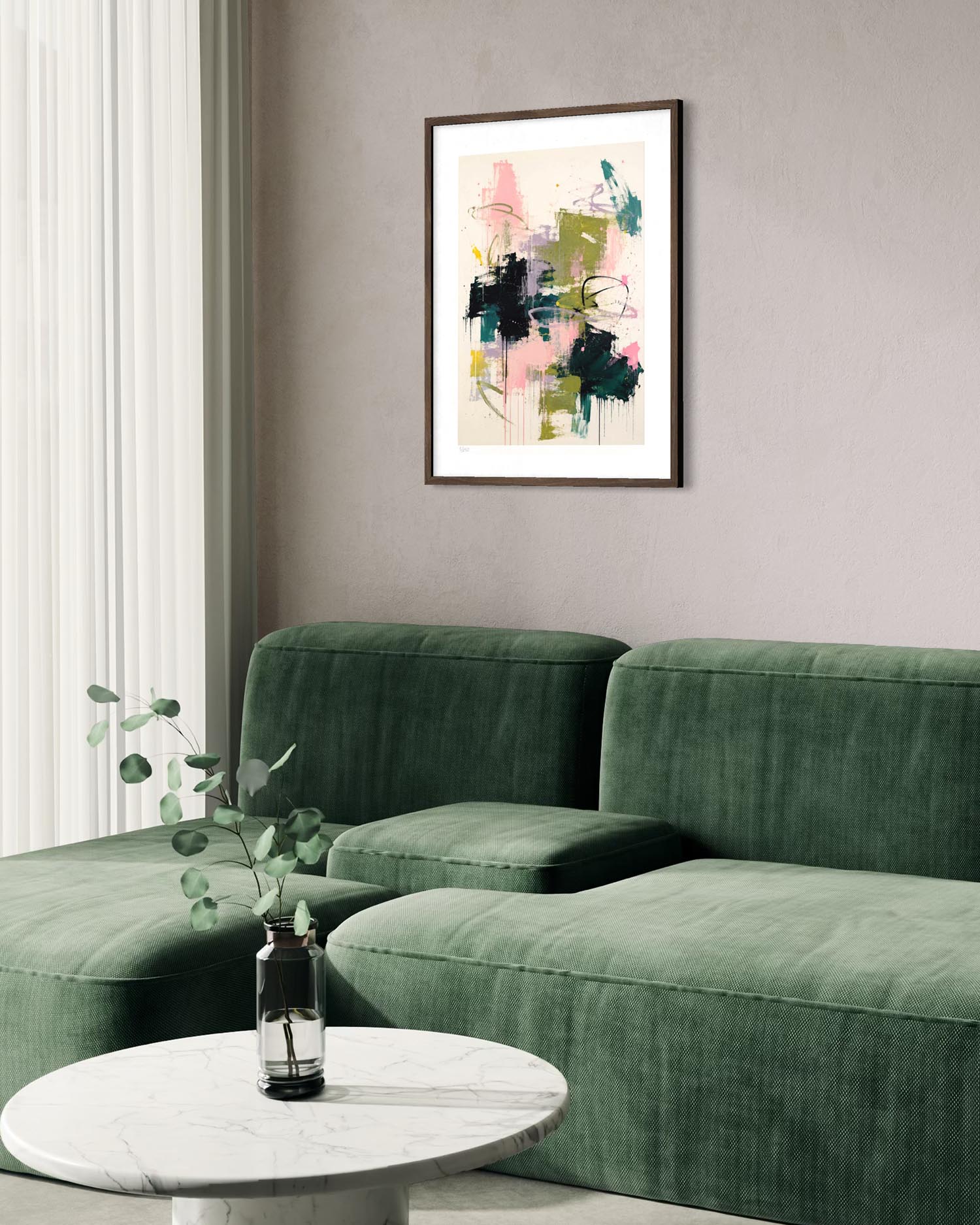 A framed abstract art print with pink, green, and black brushstrokes hangs on a gray wall above a green velvet sectional sofa, with a small round marble coffee table in the foreground.