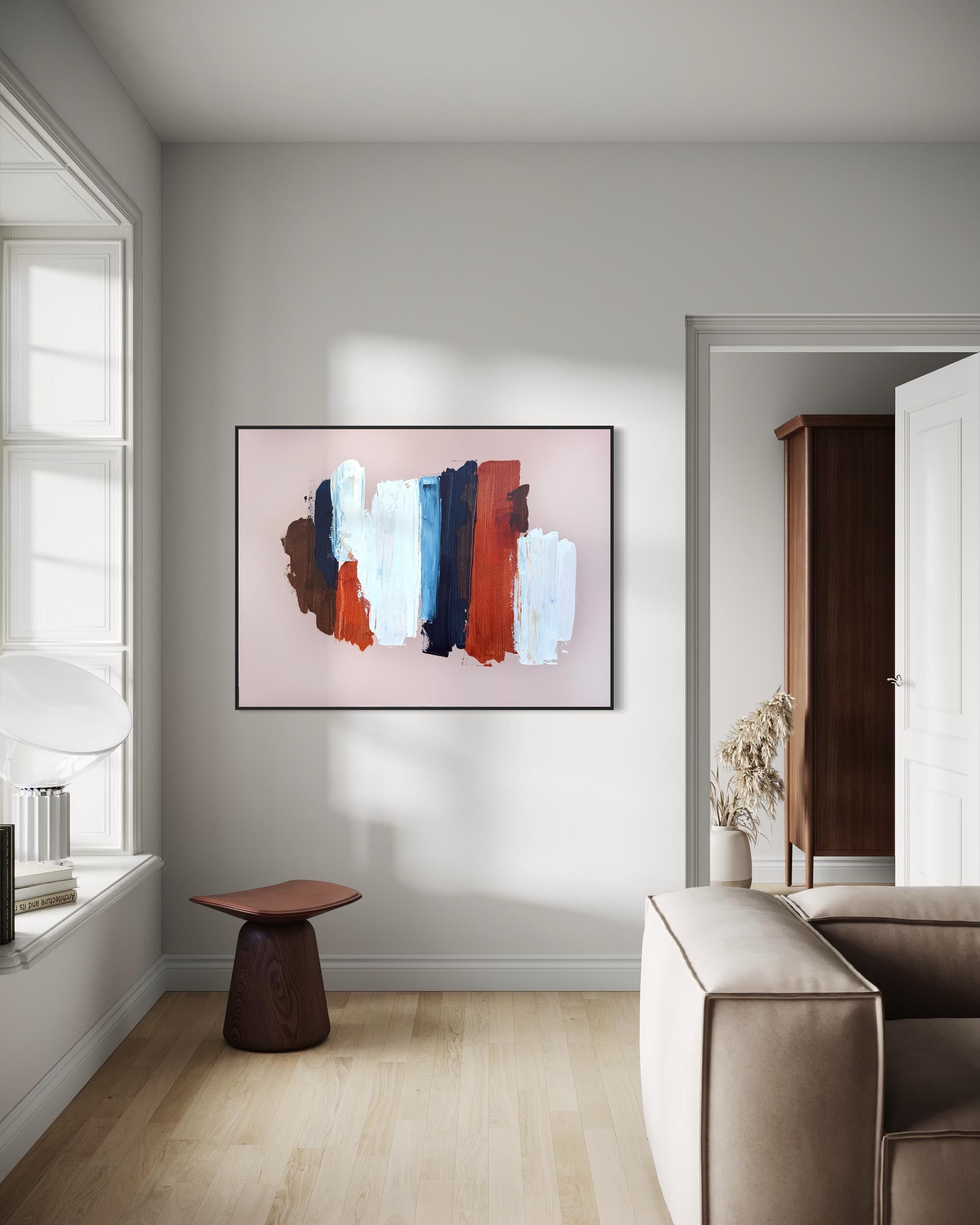 An abstract framed wall art print hangs on a light gray wall in a modern living room setting with a beige sofa, a small wooden stool, and light wood flooring.