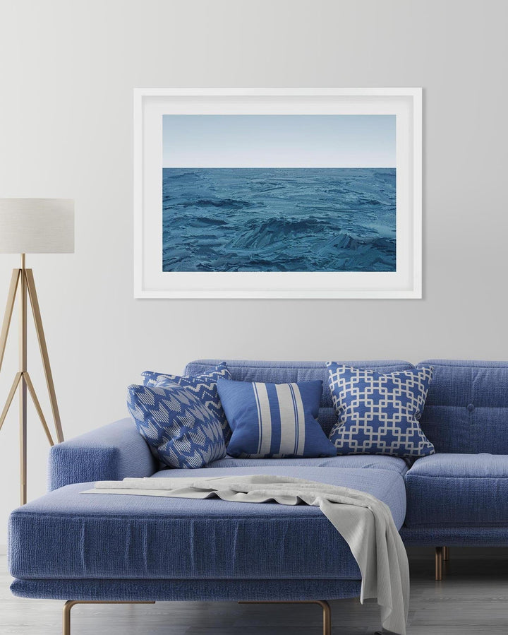 Framed artwork of a blue ocean scene above a blue sofa with patterned cushions.