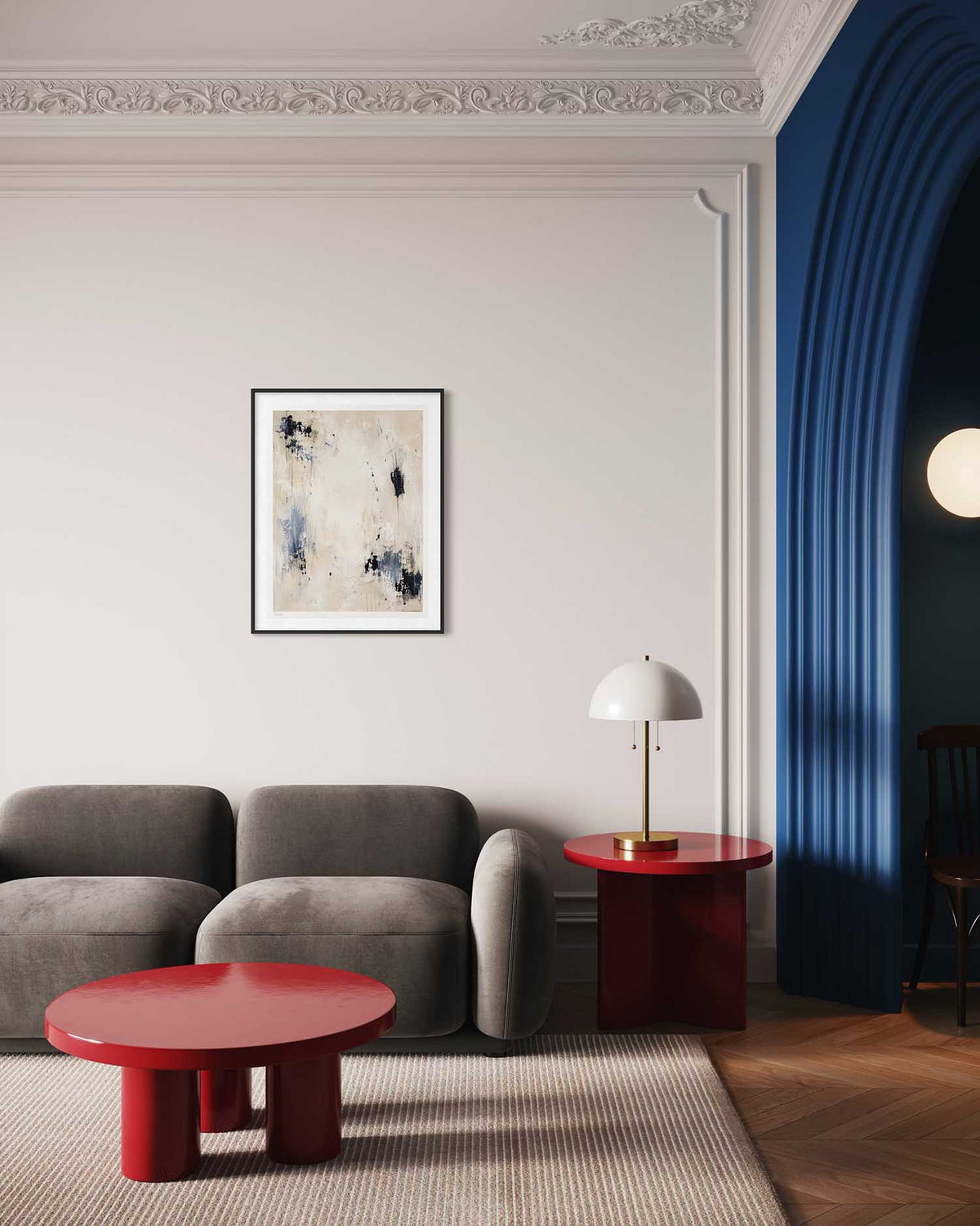 A modern living room scene featuring a framed abstract art print on a white wall above a gray sofa. The print has a black frame and displays a textured abstract design in cream, black, and blue-gray.