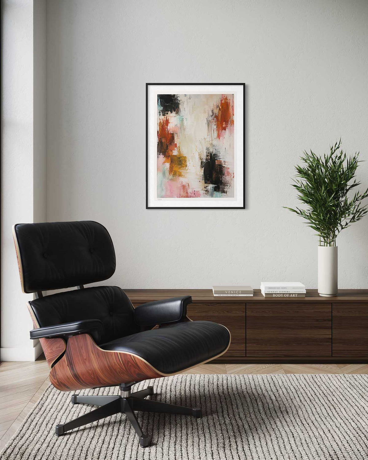 An abstract framed wall art print hangs on a light gray wall above a dark wood console, with a black lounge chair in the foreground and a potted plant to the right.