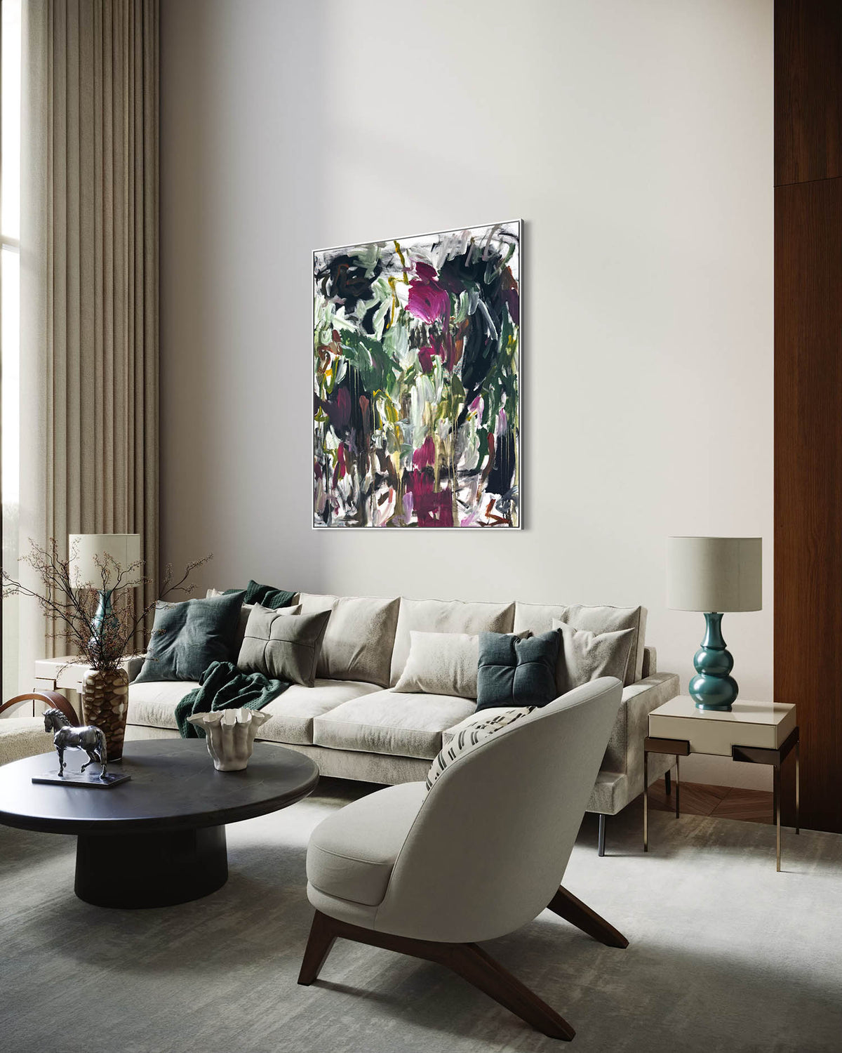 A framed abstract painting with black, green, and magenta brushstrokes hangs on a light gray wall in a modern living room setting with a beige sofa, armchair, and side tables.