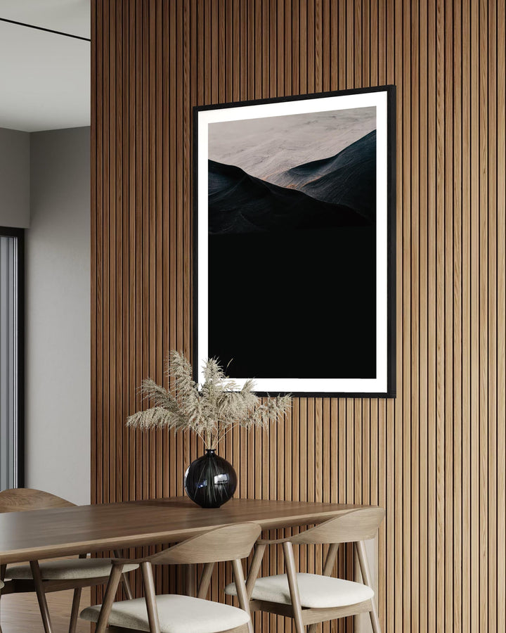 Framed mountain landscape print on a wooden wall above a dining table with decor.