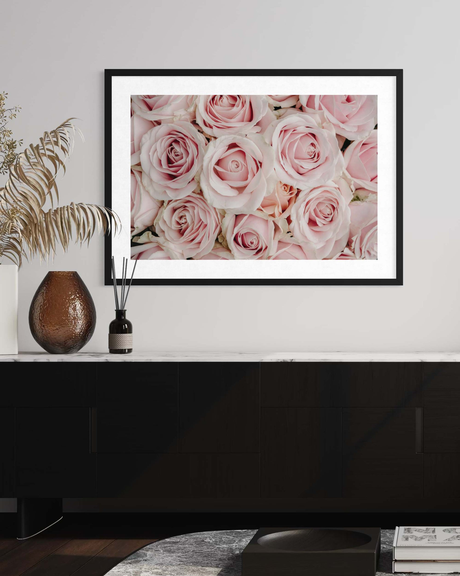 Framed picture of pink roses on a wall above a black cabinet.