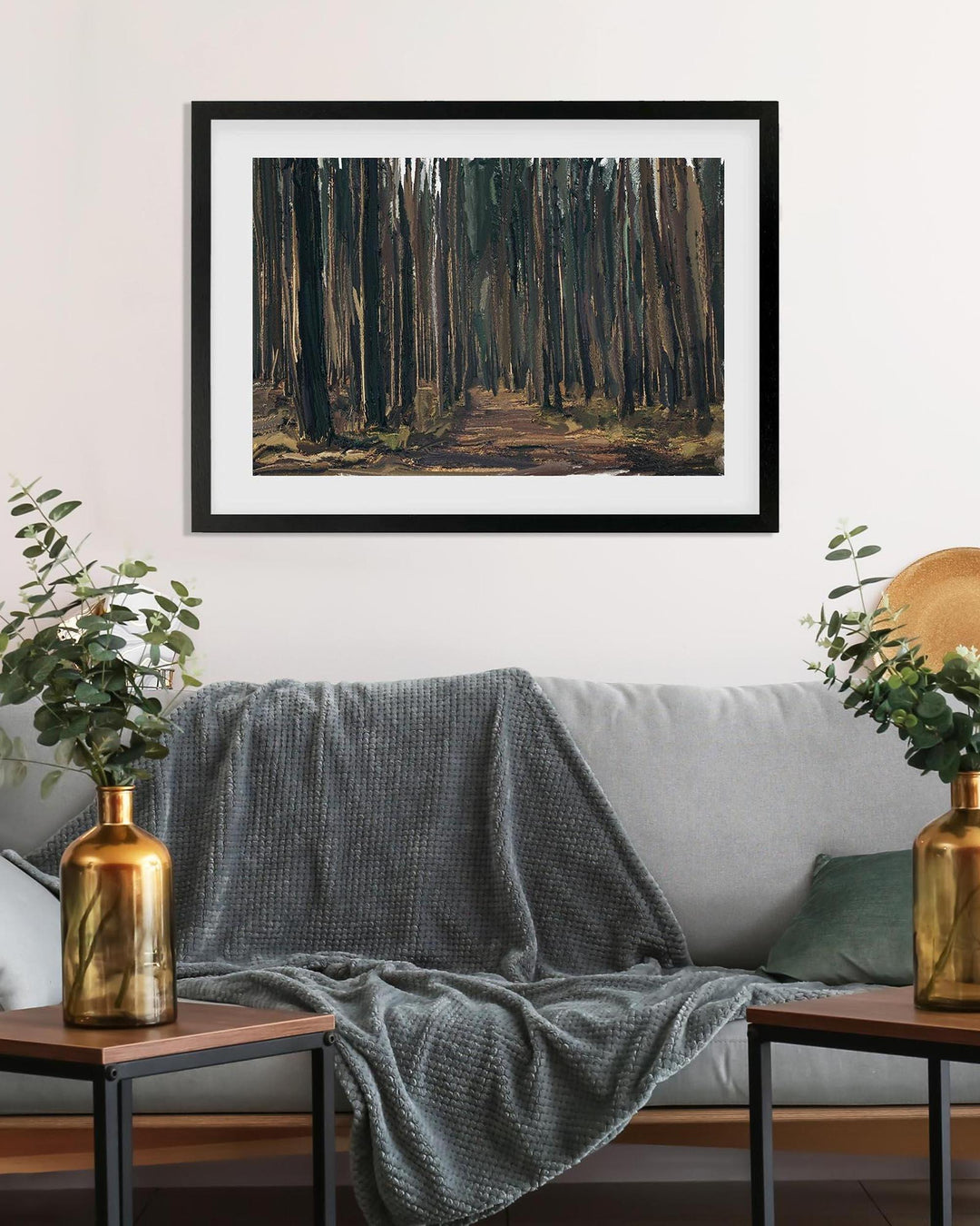 Framed artwork of a forest scene above a gray sofa with decorative elements.