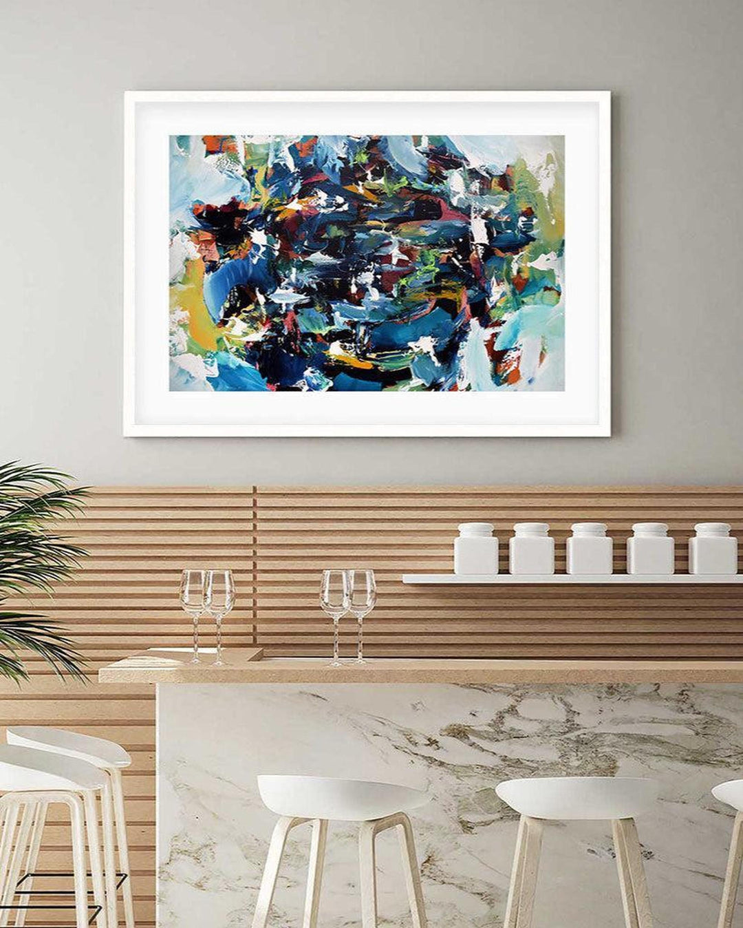 Abstract painting in a white frame above a kitchen counter with stools.