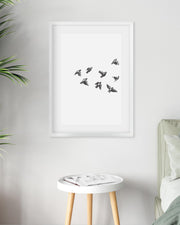 Framed artwork of birds on a white wall above a small table with a plant and bed.