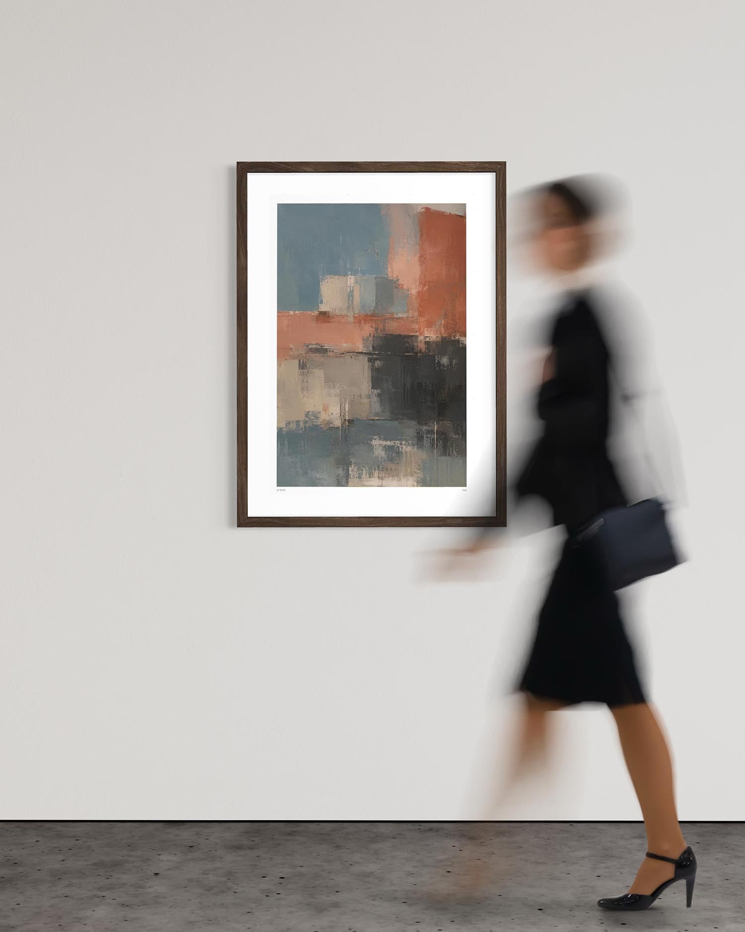 A framed abstract art print with blue, gray, and terracotta brushstrokes hangs on a white gallery wall. A woman in a black dress and heels walks past the frame on the right, creating a motion blur effect.