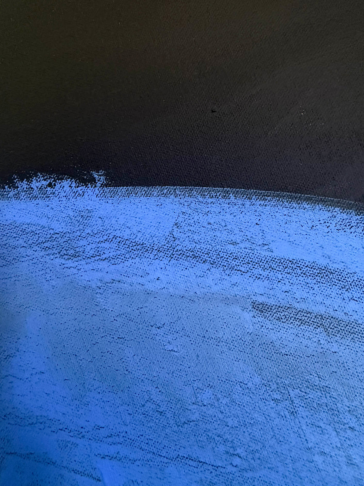 A close-up of a textured surface showing a horizontal brushstroke transition from dark charcoal/black at the top to bright periwinkle blue at the bottom.