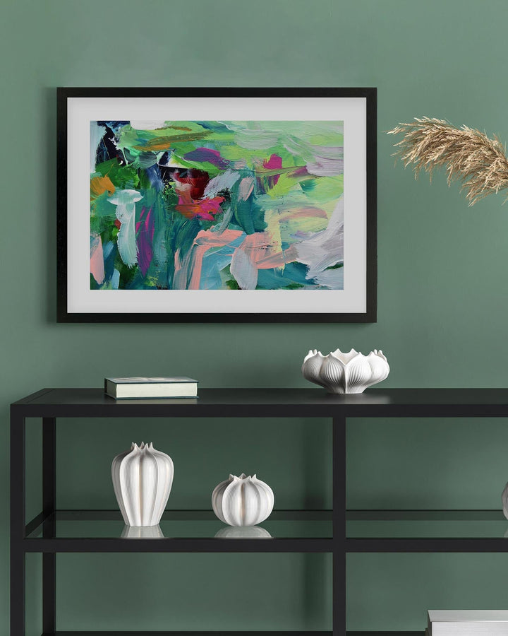 Framed abstract painting on a green wall above a black shelf with decorative items.