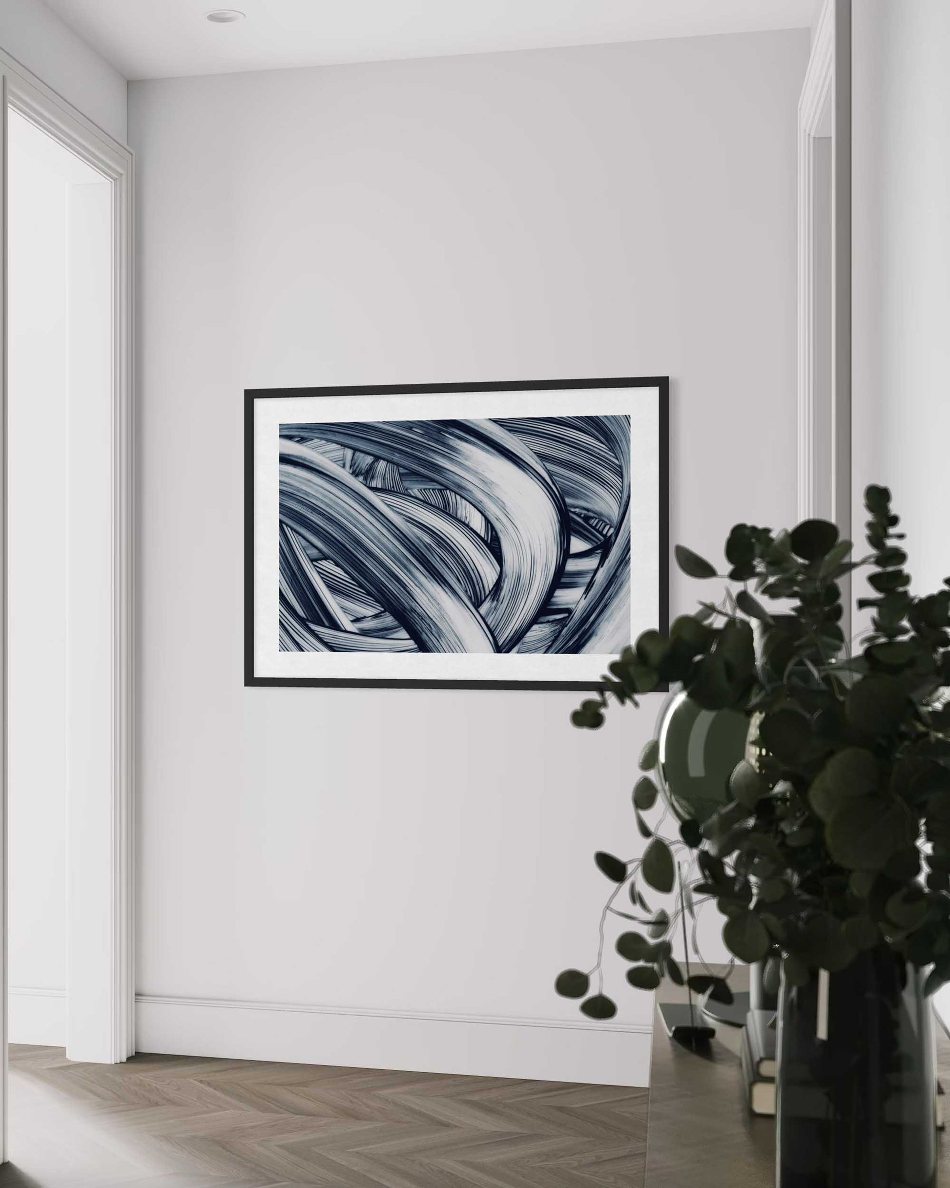 Framed abstract art on a white wall with a plant in the foreground
