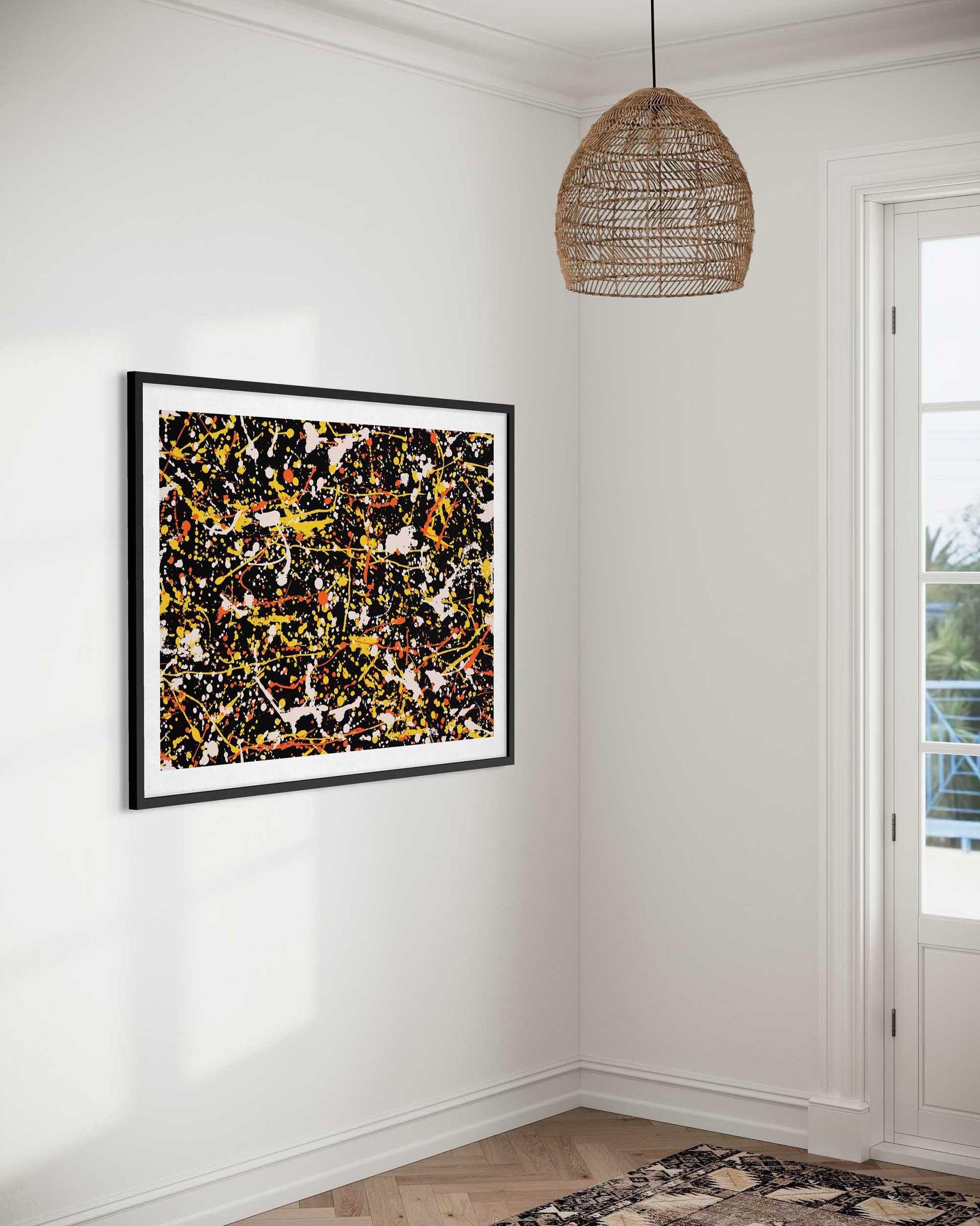 Abstract art piece in a black frame on a white wall with a woven pendant light.
