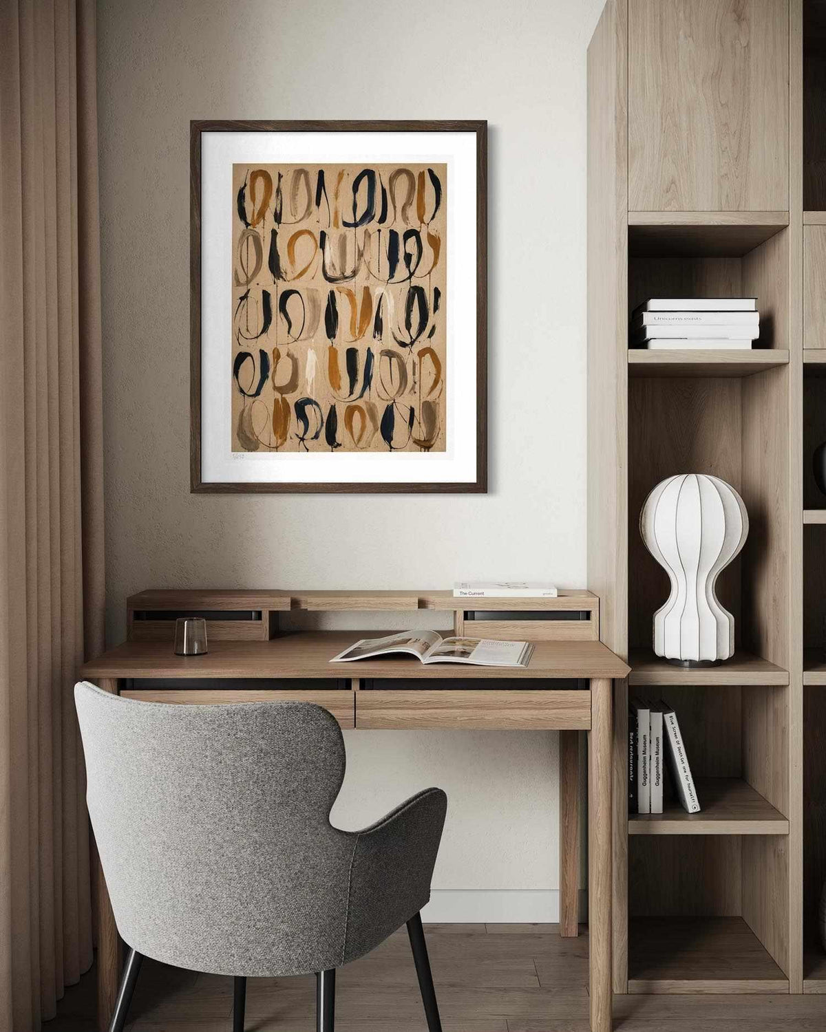 A framed abstract art print with organic flowing lines in beige, brown, and black hangs on a light gray wall above a wooden desk with a gray upholstered chair. The room includes a wooden shelving unit with books and a white sculptural vase.