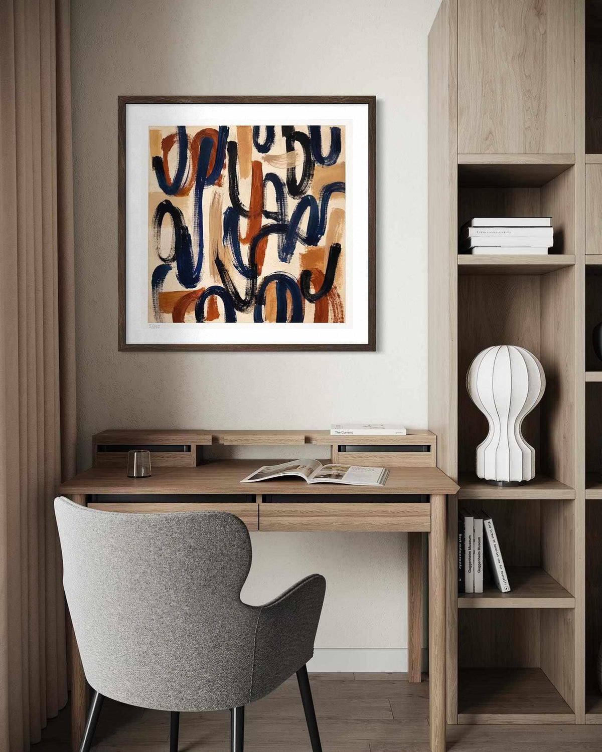 A framed abstract art print featuring navy blue and terracotta brushstrokes on a warm beige background, styled in a modern home office setting above a wooden desk with a gray chair.