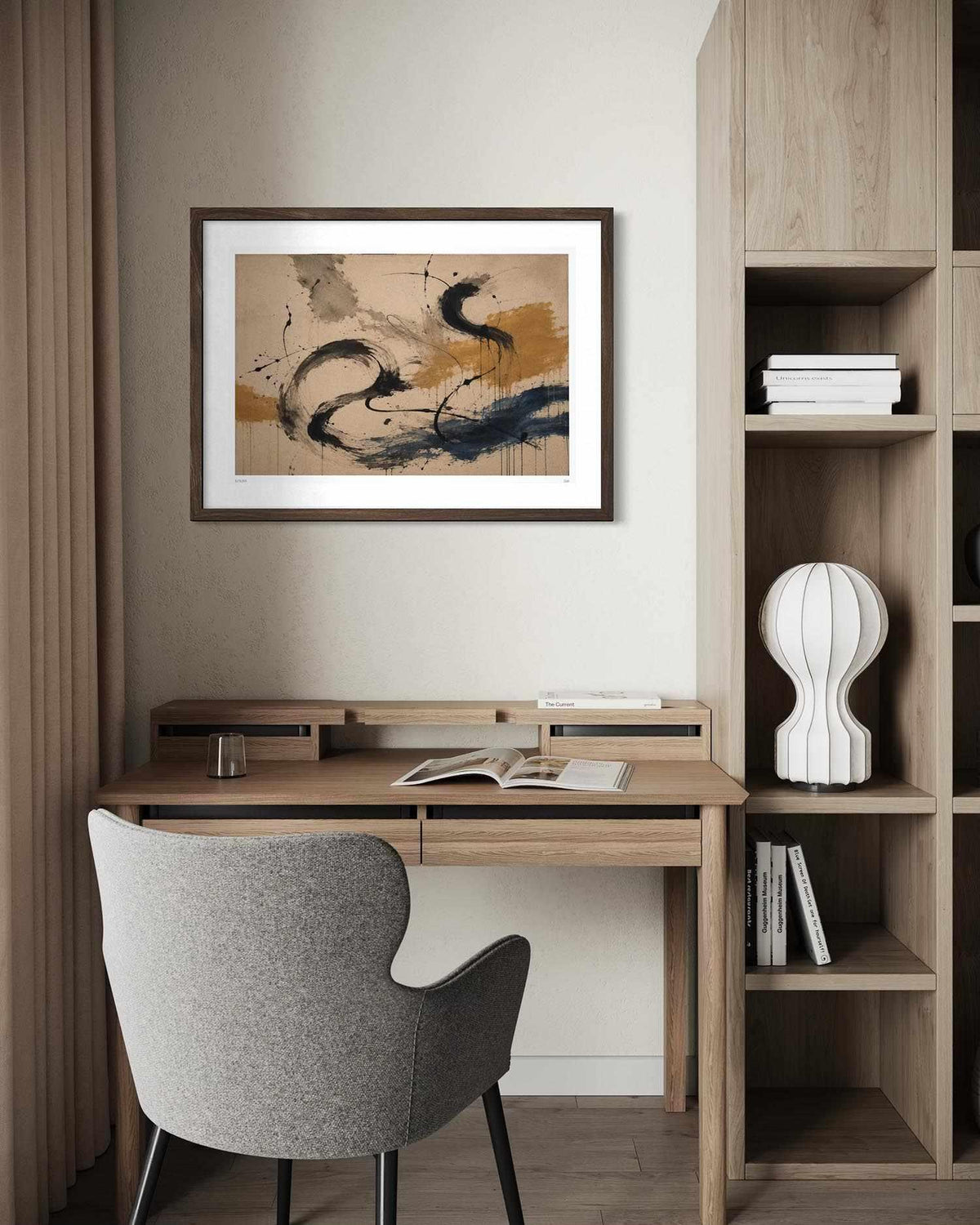 A framed abstract art print with black, blue, and gold brushstrokes on a beige background, displayed on a wall above a wooden desk with a gray chair in a modern home office setting.