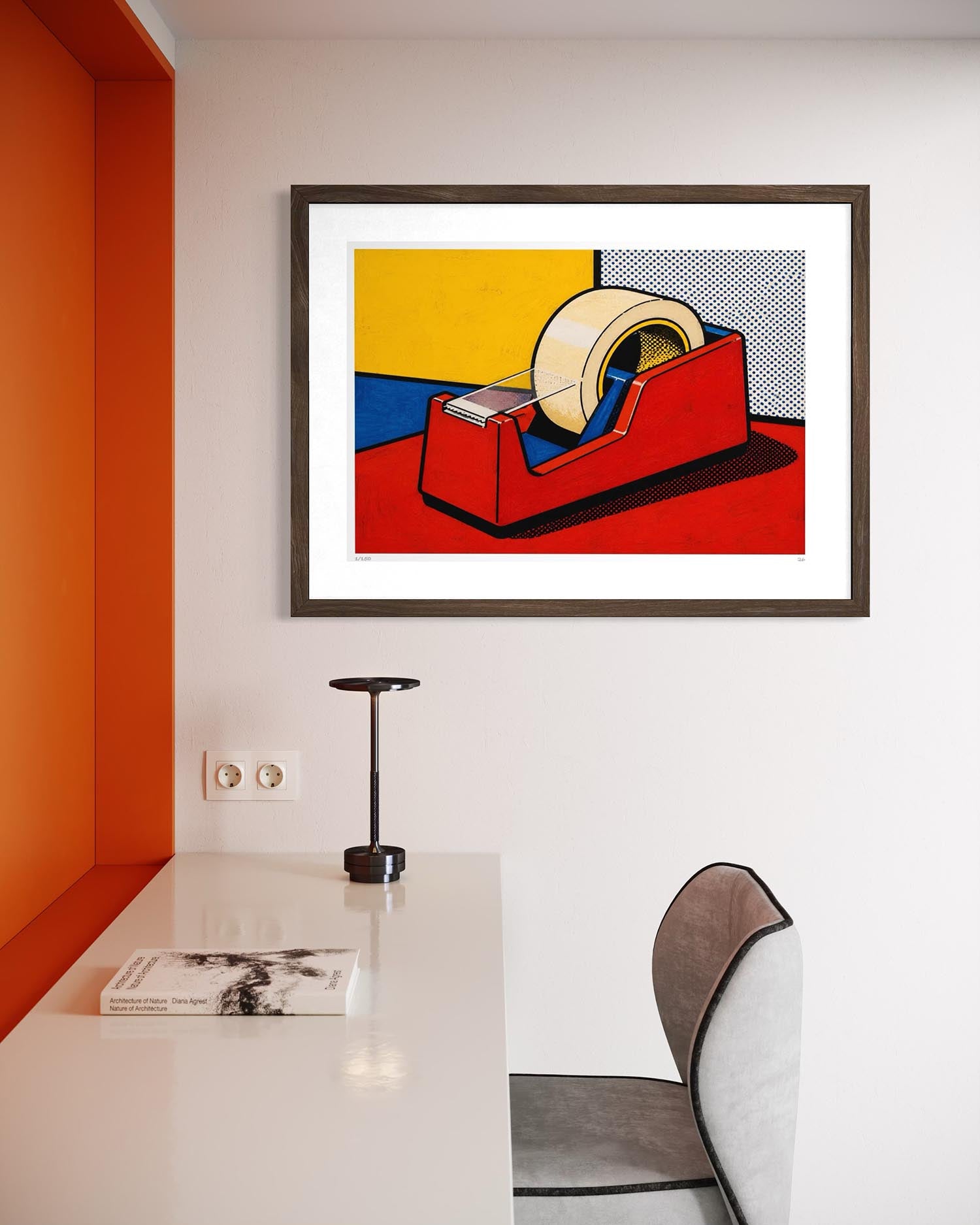 A framed pop art print of a tape dispenser, styled on a white wall above a modern desk with a lamp and chair.