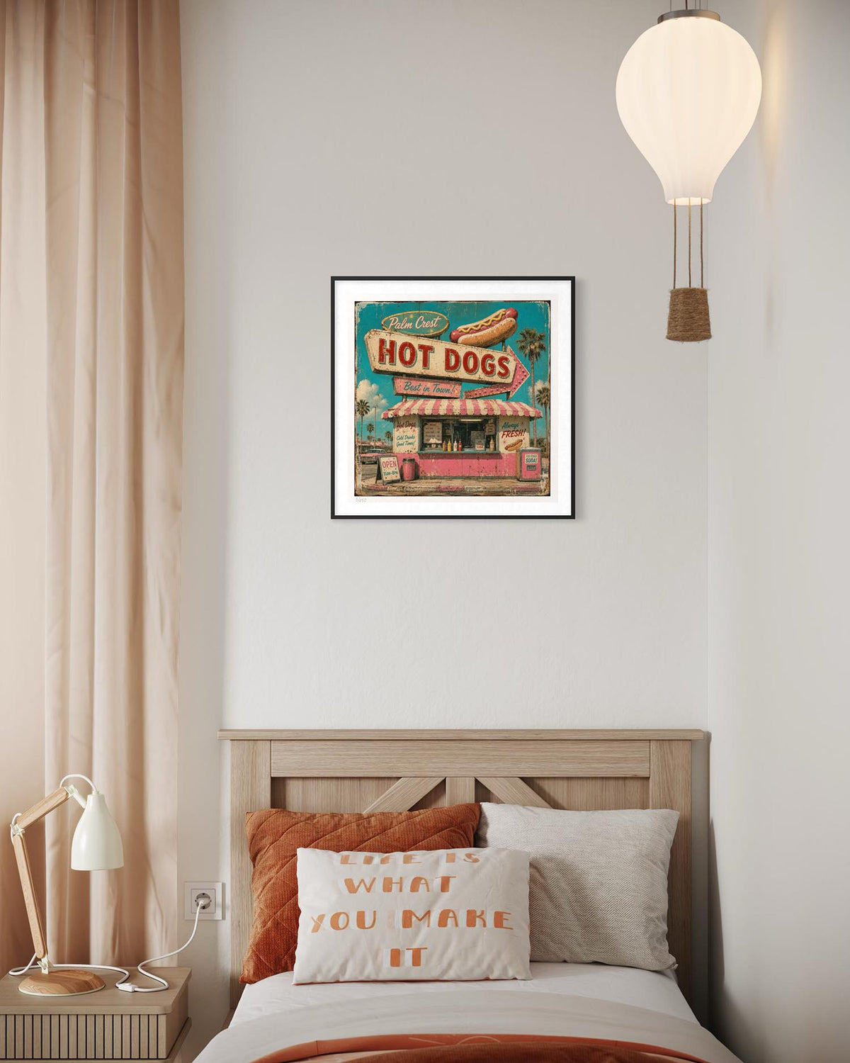 A framed art print of a retro hot dog stand hangs on a light gray wall above a bed with orange and white pillows in a modern bedroom setting.