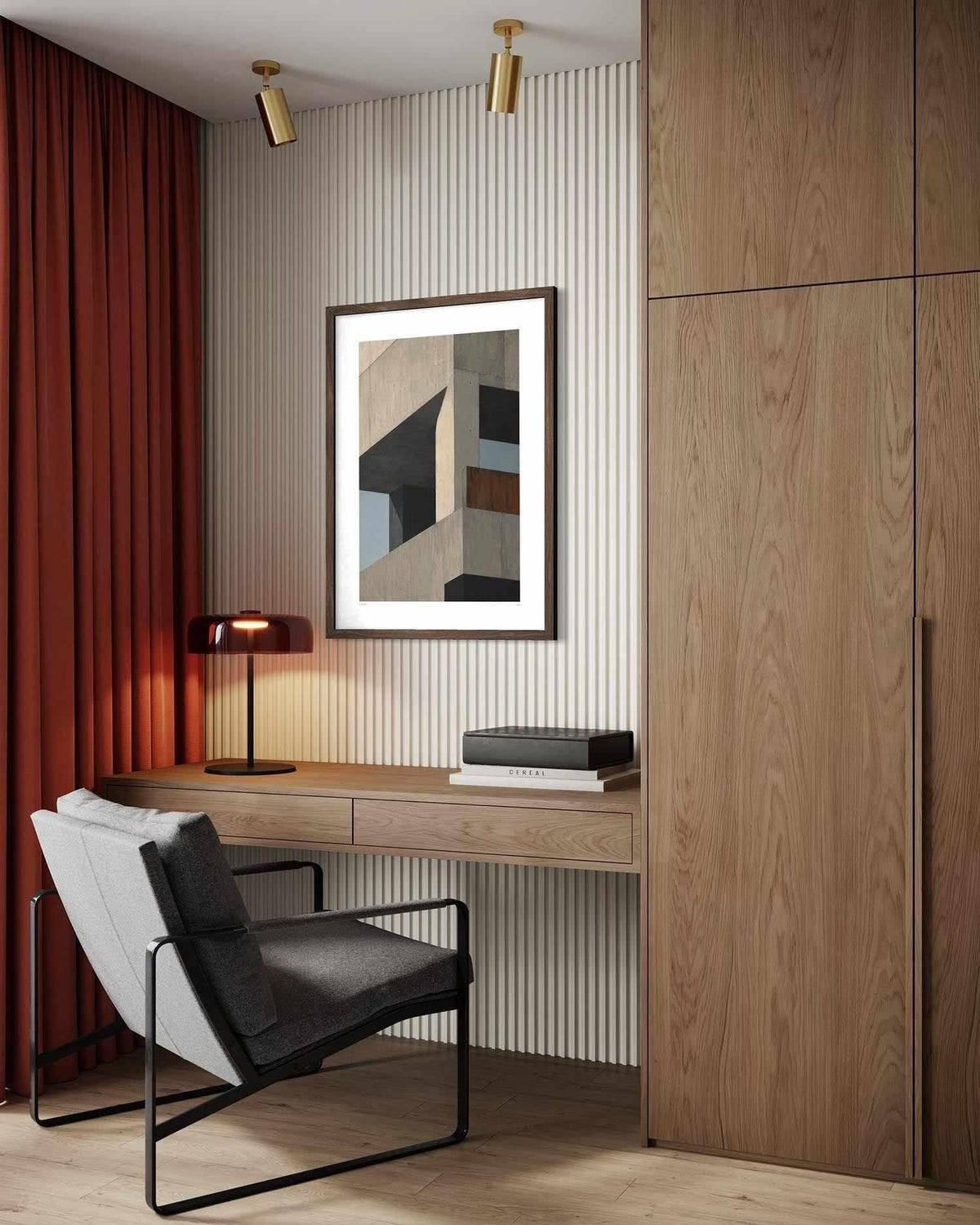A framed abstract geometric art print hangs on a ribbed cream wall above a wooden desk in a modern home office. The room features a light wood cabinet, a gray and white accent chair, a lit black table lamp, and a deep red curtain on the left.