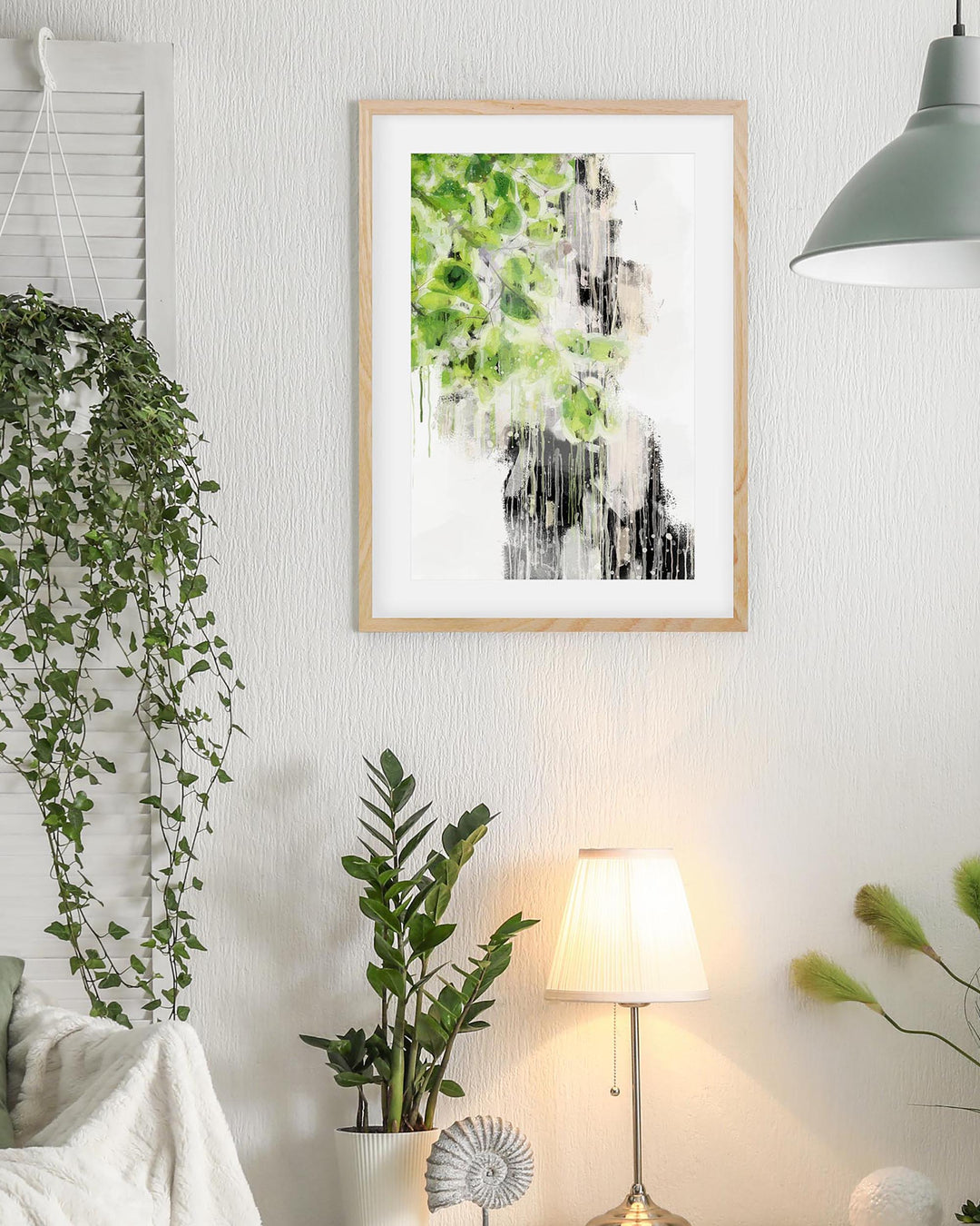 Framed artwork of a waterfall with greenery on a wall in a room with plants and a lamp.