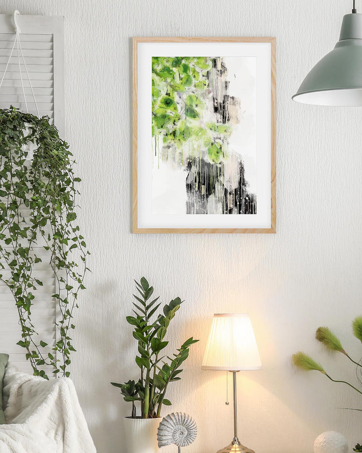 Framed artwork of a waterfall with greenery on a wall in a room with plants and a lamp.