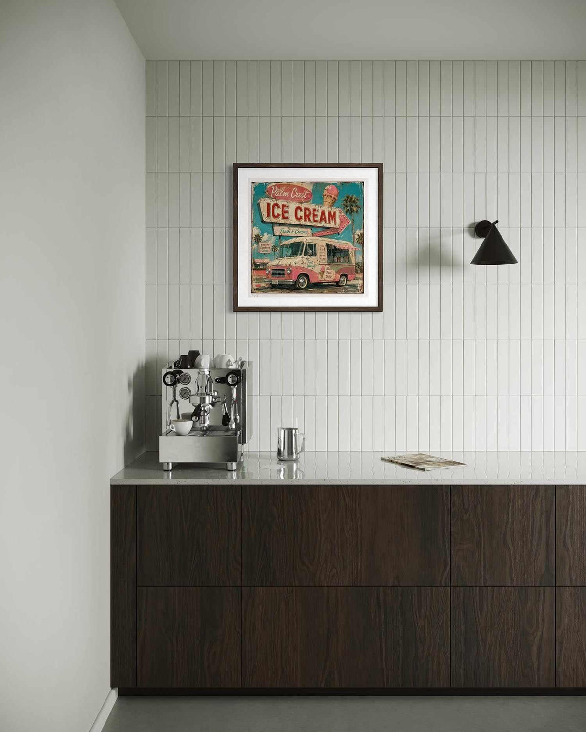A framed vintage-style ice cream truck poster hangs on a white tiled wall above a dark wood counter with a stainless steel espresso machine and a small metal cup in a minimalist interior setting.