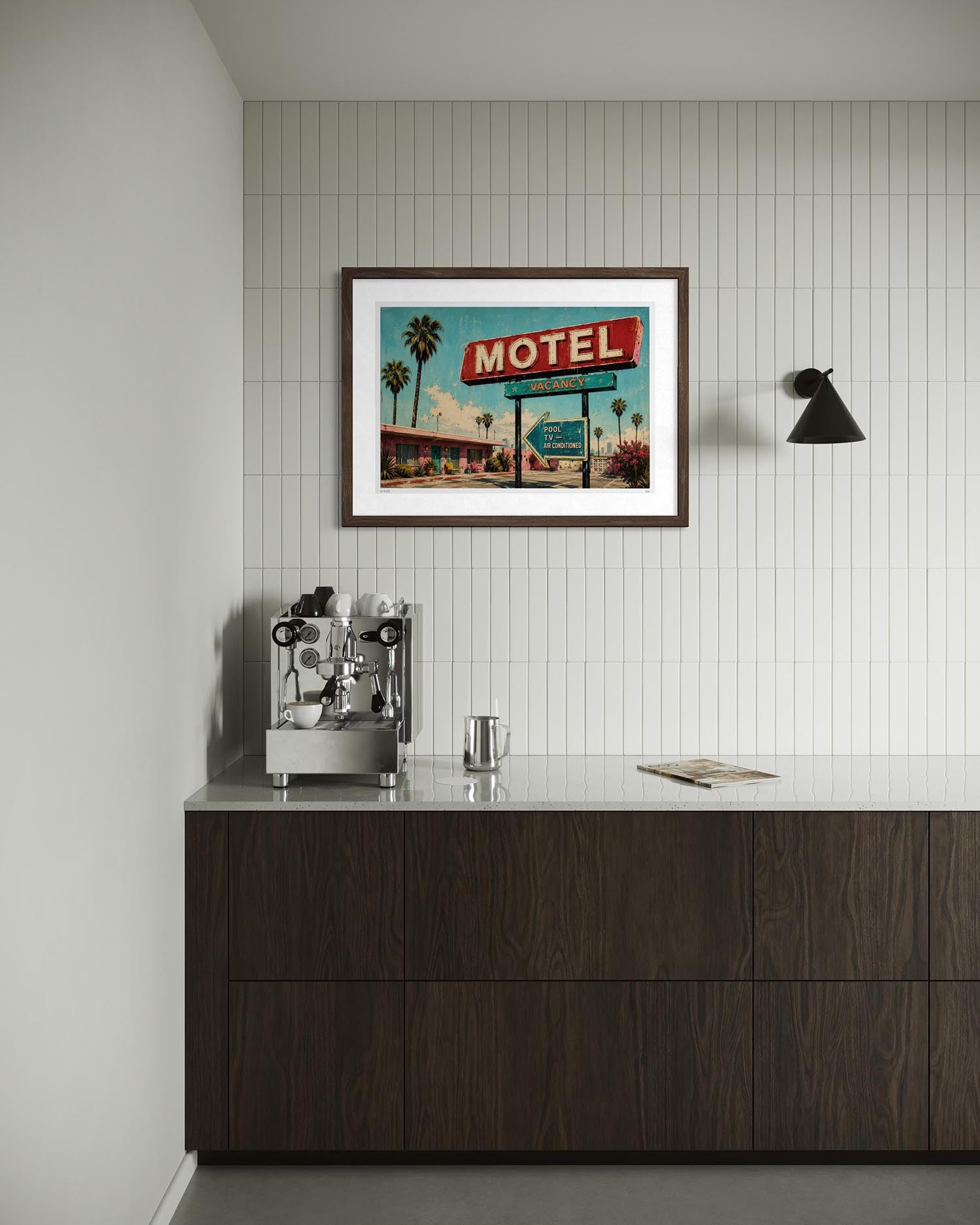 A framed art print of a retro 'Motel' sign hanging on a white tiled wall above a dark wood counter with a coffee machine.