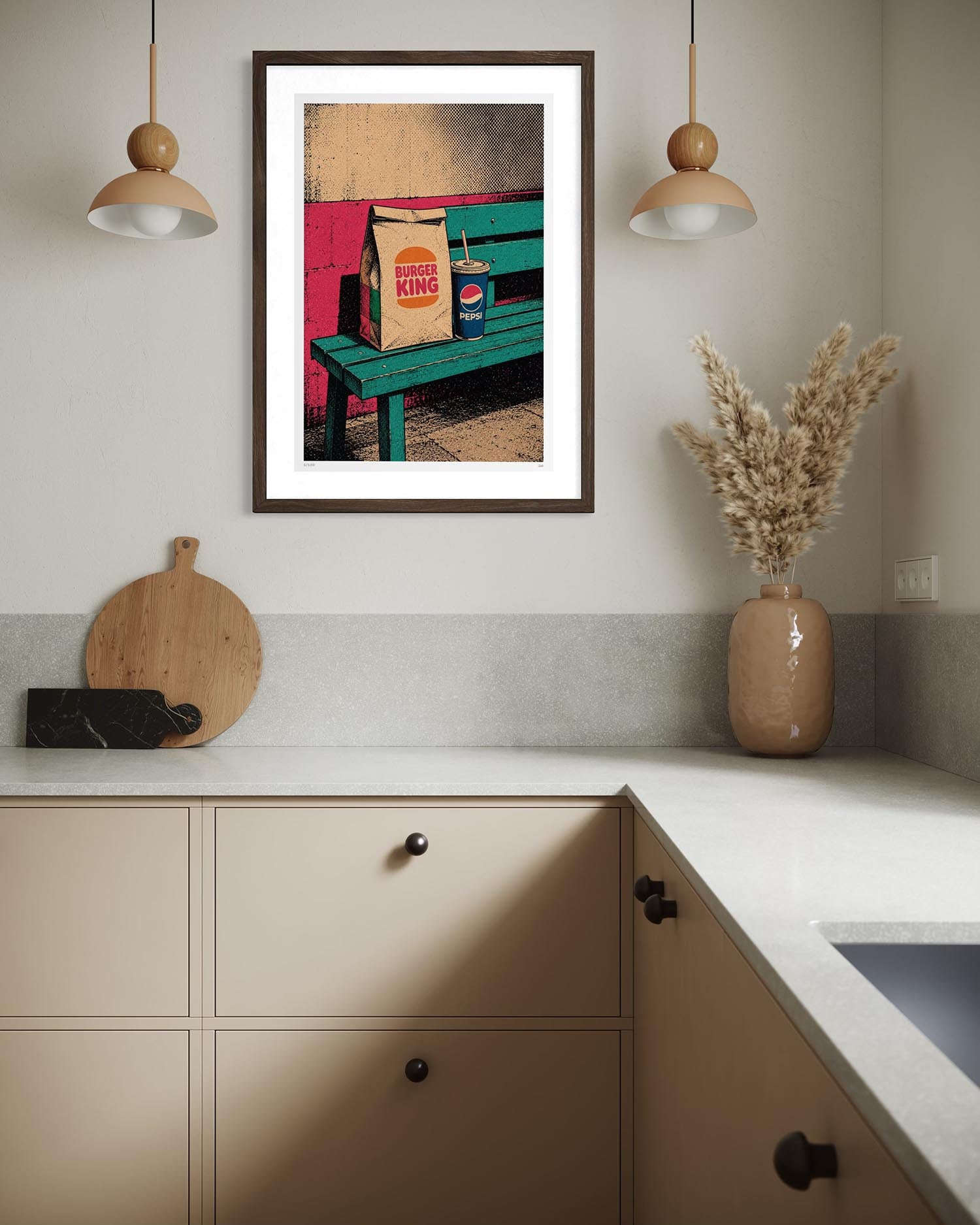 A framed art print featuring a colorful pop-art scene of a green bench with a Burger King bag and a Pepsi can, displayed on a kitchen wall above a beige countertop with decorative items.