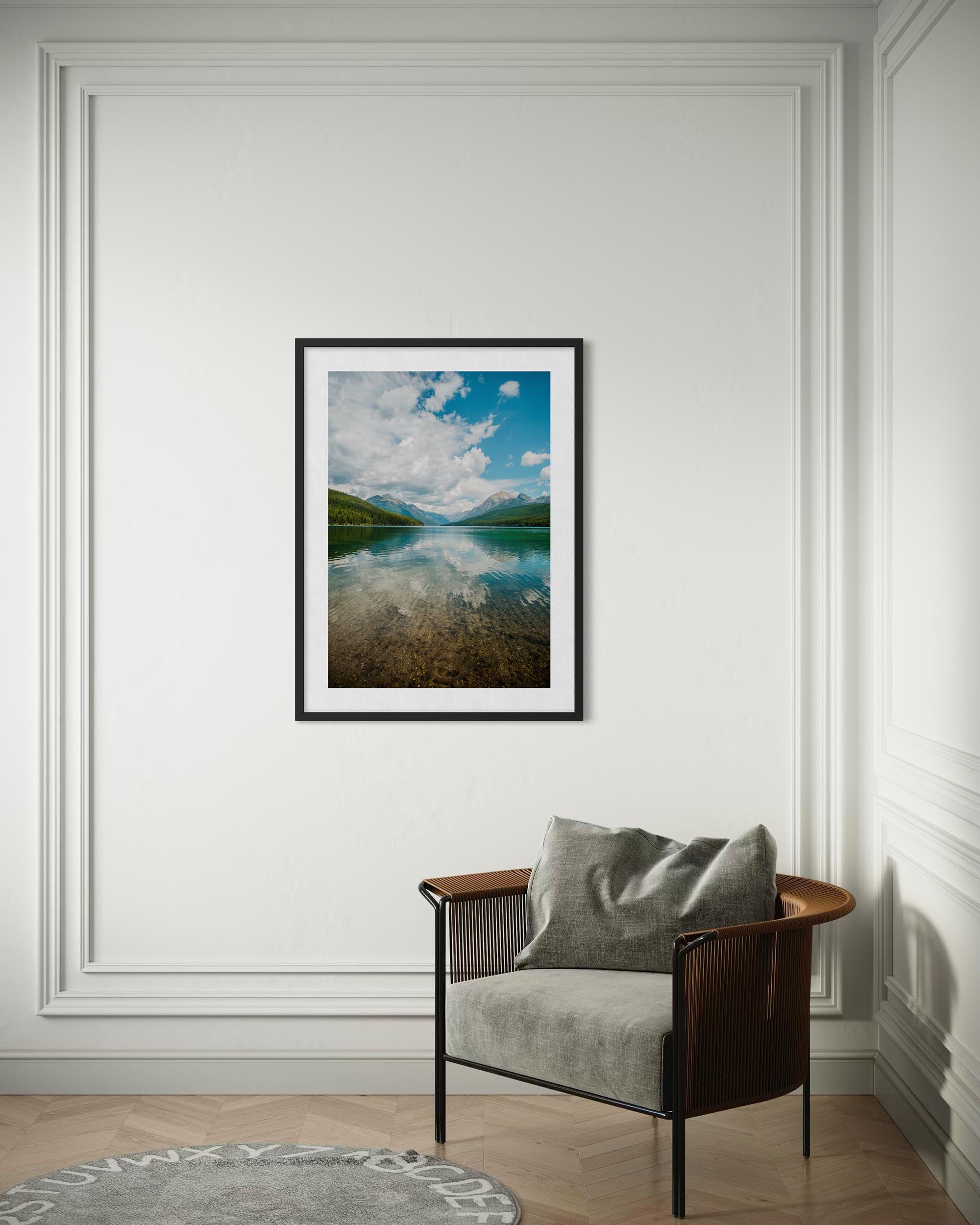 Framed landscape print on a wall above a chair with a cushion.