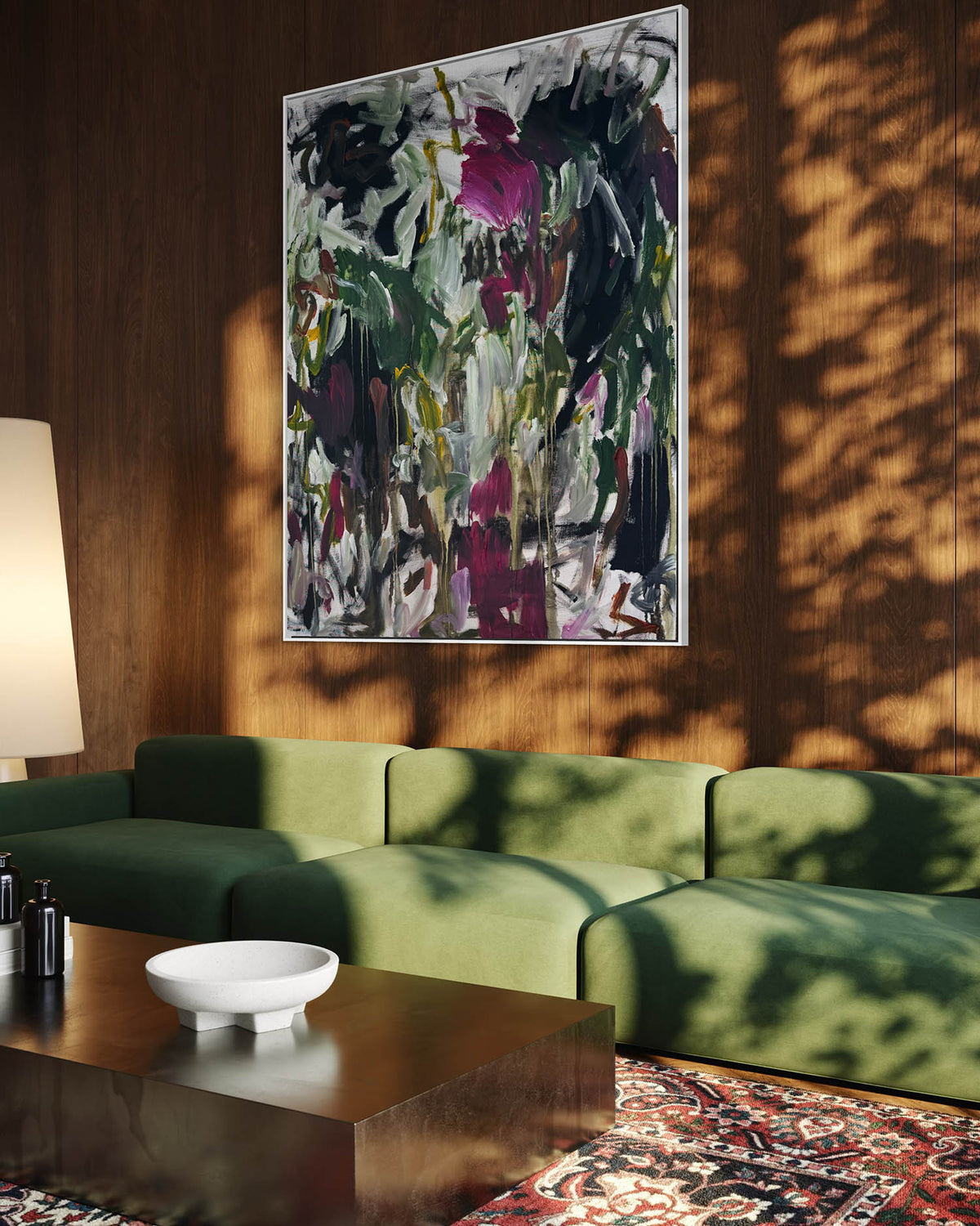 An abstract floral canvas painting with green, black, and magenta brushstrokes, displayed on a dark wood-paneled wall above a green sectional sofa in a modern living room setting.