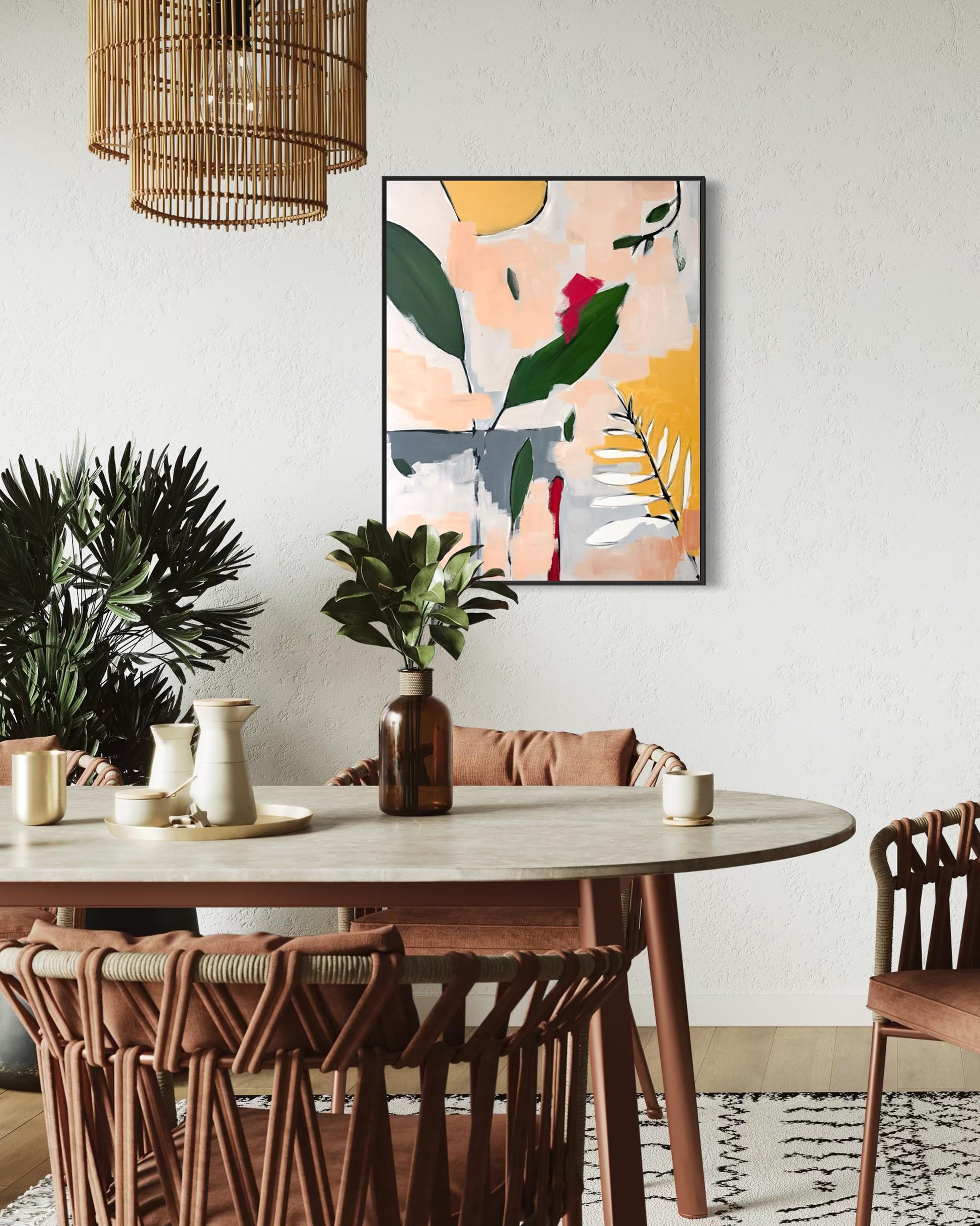 An abstract botanical wall art print with green leaves, yellow shapes, and a pink background, hanging on a white wall above a dining table with woven chairs and plants.