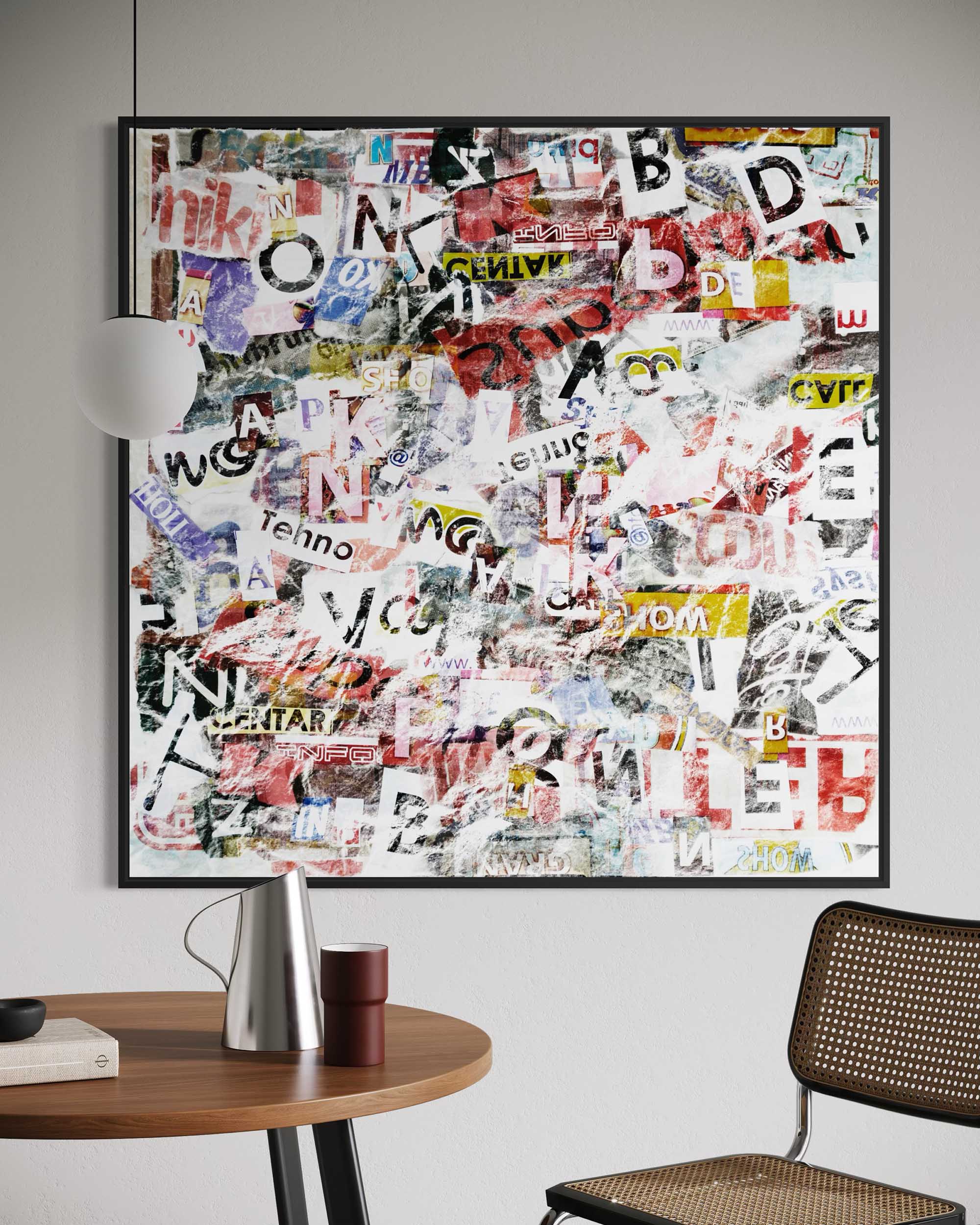 Framed collage of colorful text and graphics on a wall above a table and chair.