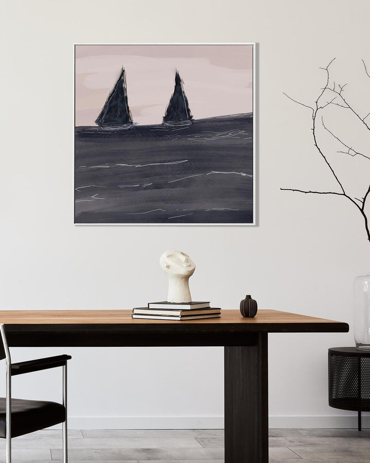 Framed abstract art of sailboats on a wall above a wooden table.