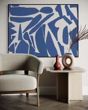 Modern living room with abstract blue artwork, beige armchair, and side table with decorative vases.