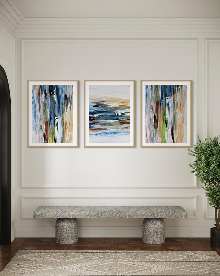Three abstract paintings on a wall above a stone bench in a room with a plant.
