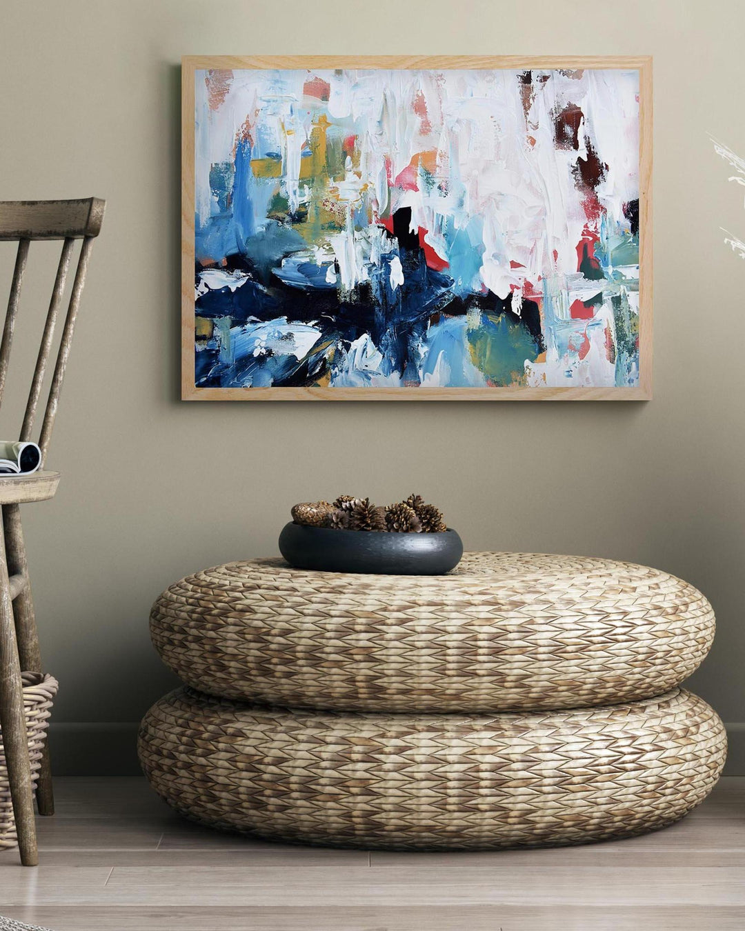 Abstract painting on a wall above a woven ottoman with a decorative bowl.