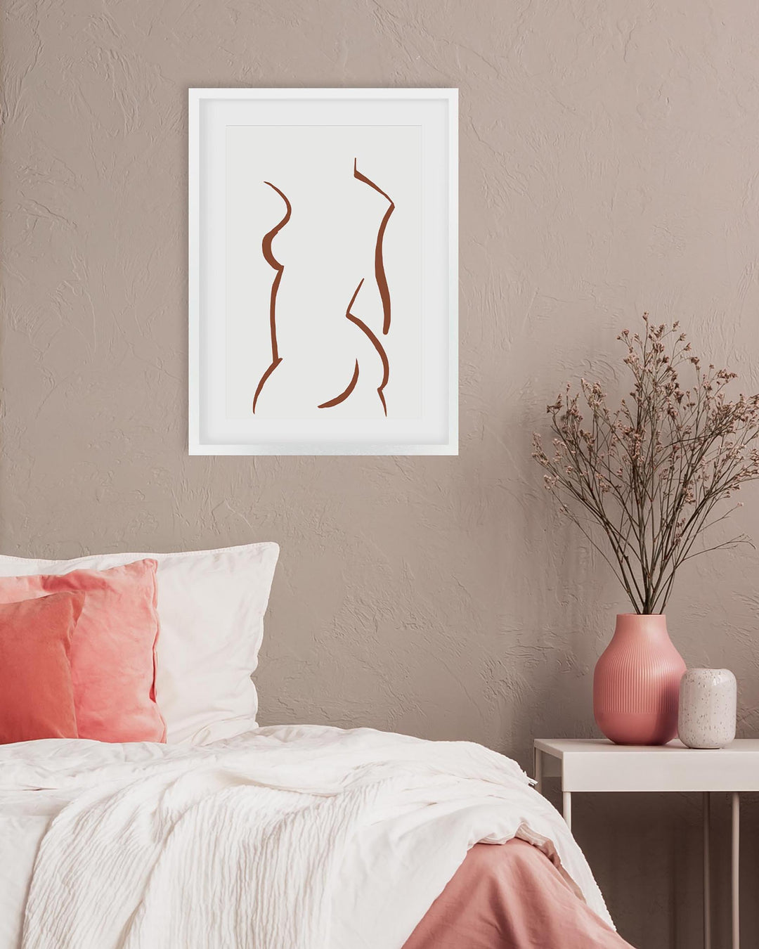 Framed abstract art above a bed with pink and white pillows and a vase on a nightstand.