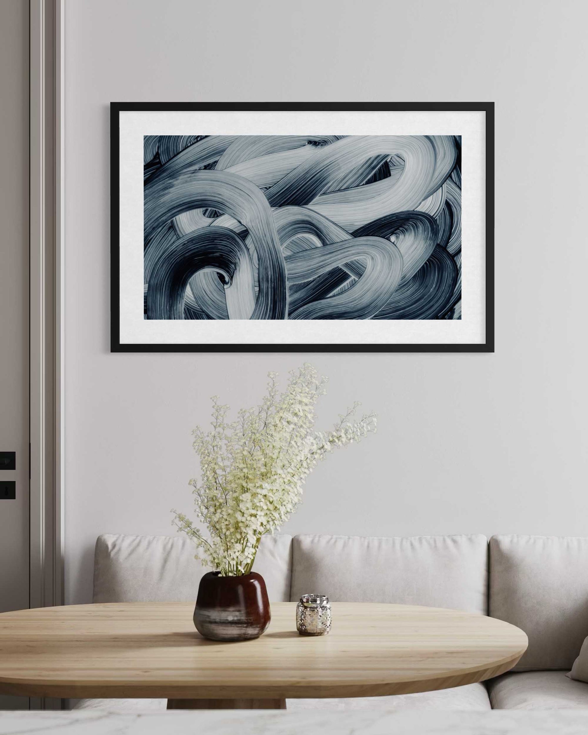 Framed abstract art piece on a wall above a wooden table with a vase and candle.
