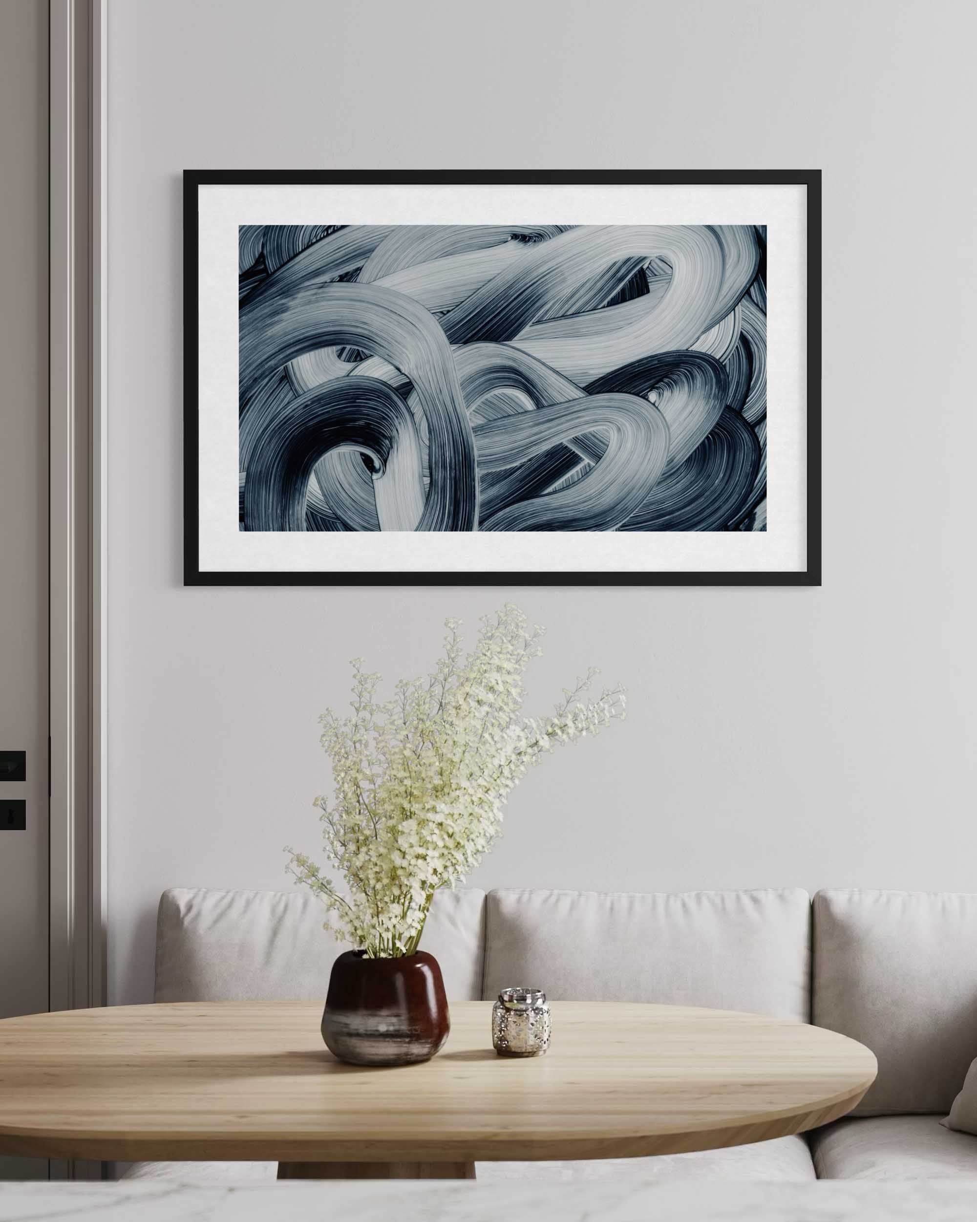 Framed abstract art piece on a wall above a wooden table with a vase and candle.