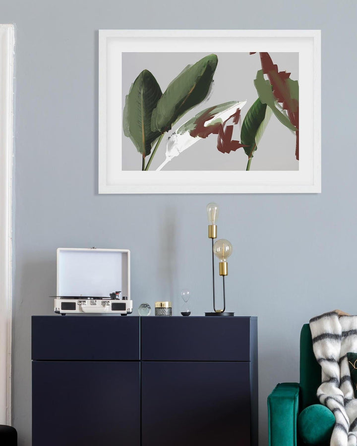 Framed artwork of leaves on a wall above a dark blue cabinet with decorative items.