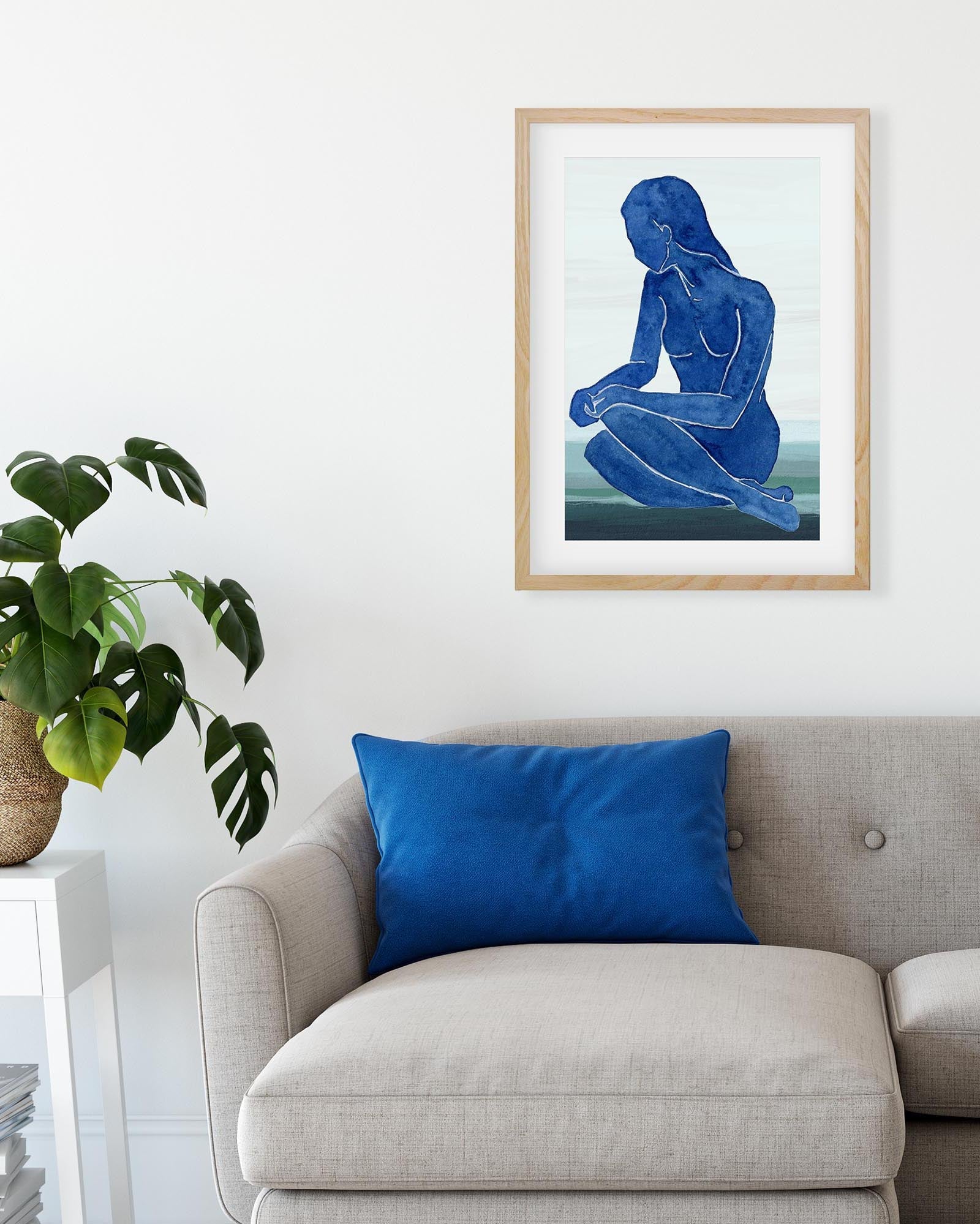 Framed artwork of a blue figure on a white wall above a beige sofa with a blue pillow.