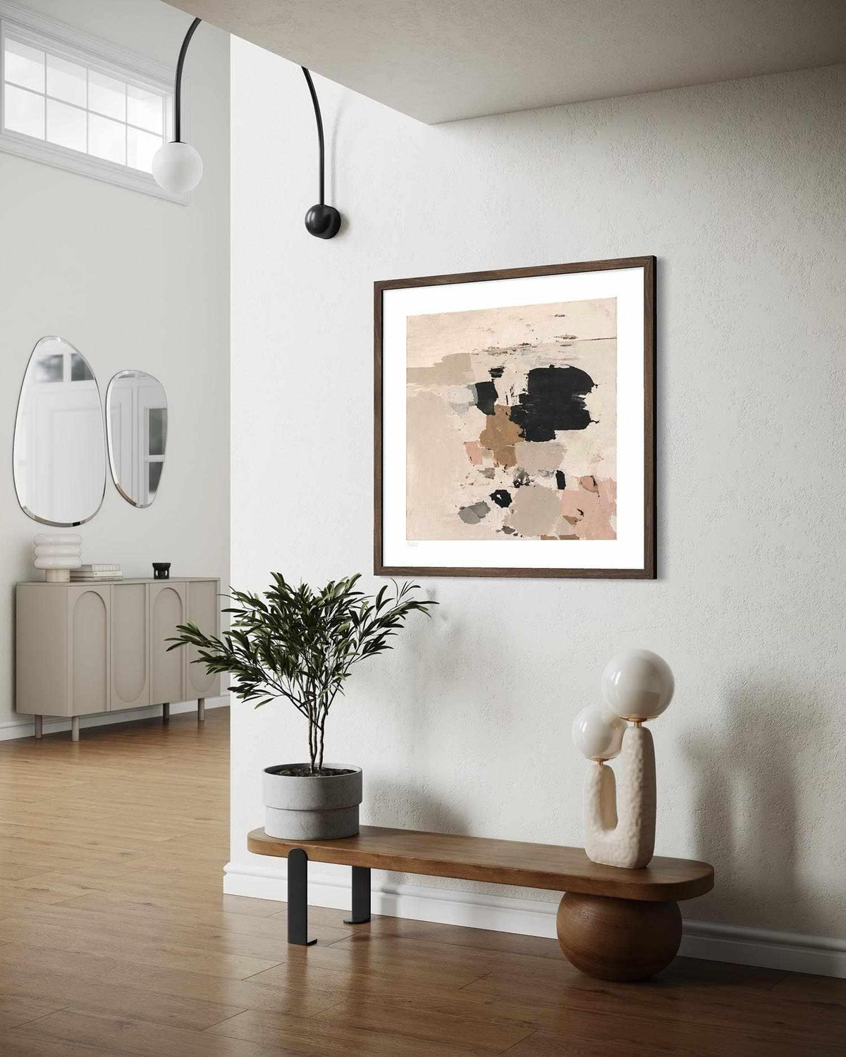 Framed abstract wall art hanging on a white wall in a modern, sunlit entryway. The artwork features an abstract composition in beige, black, and dusty pink tones with a dark brown frame.