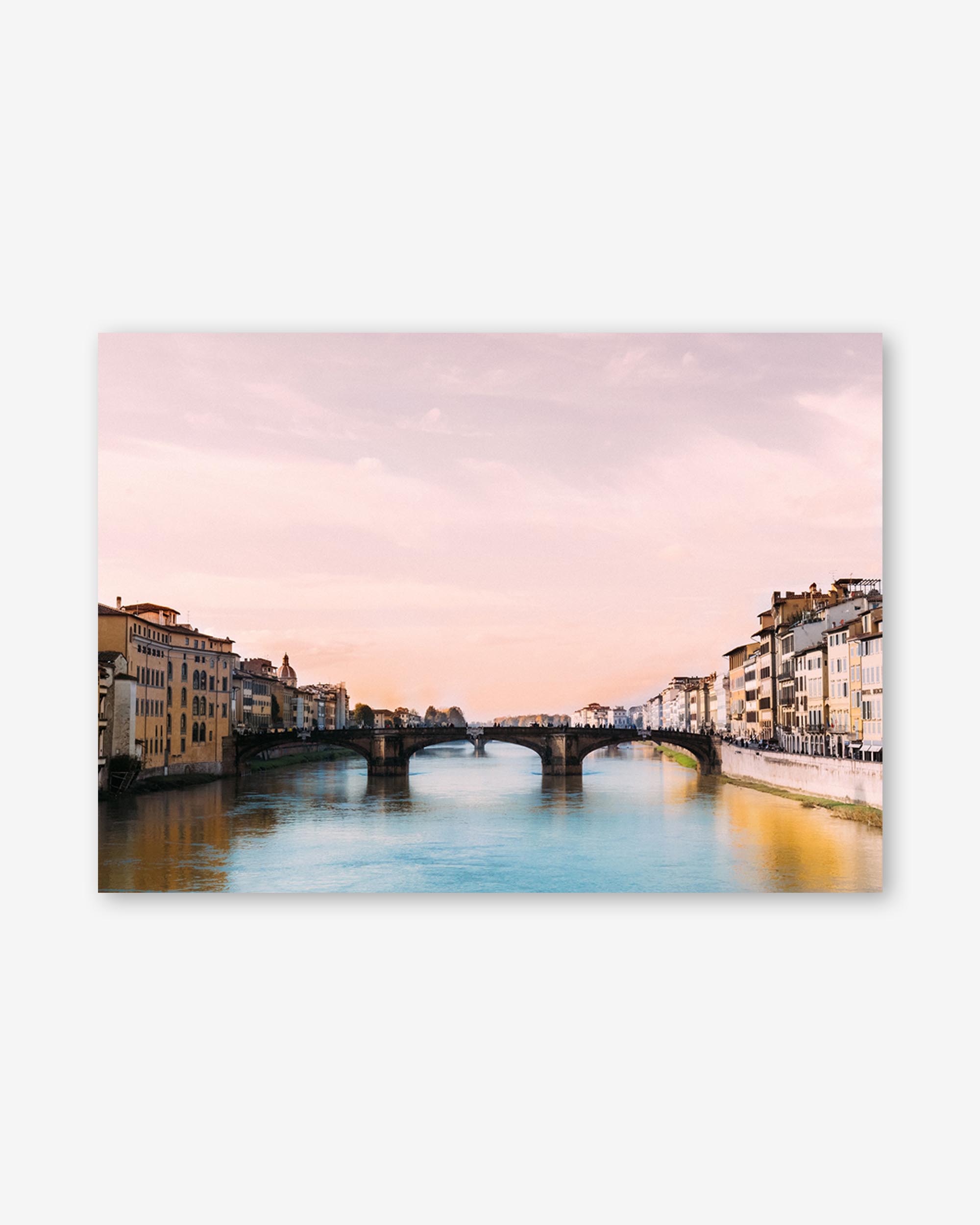 Cityscape with a bridge over a river at sunset, with pink and orange hues in the sky.